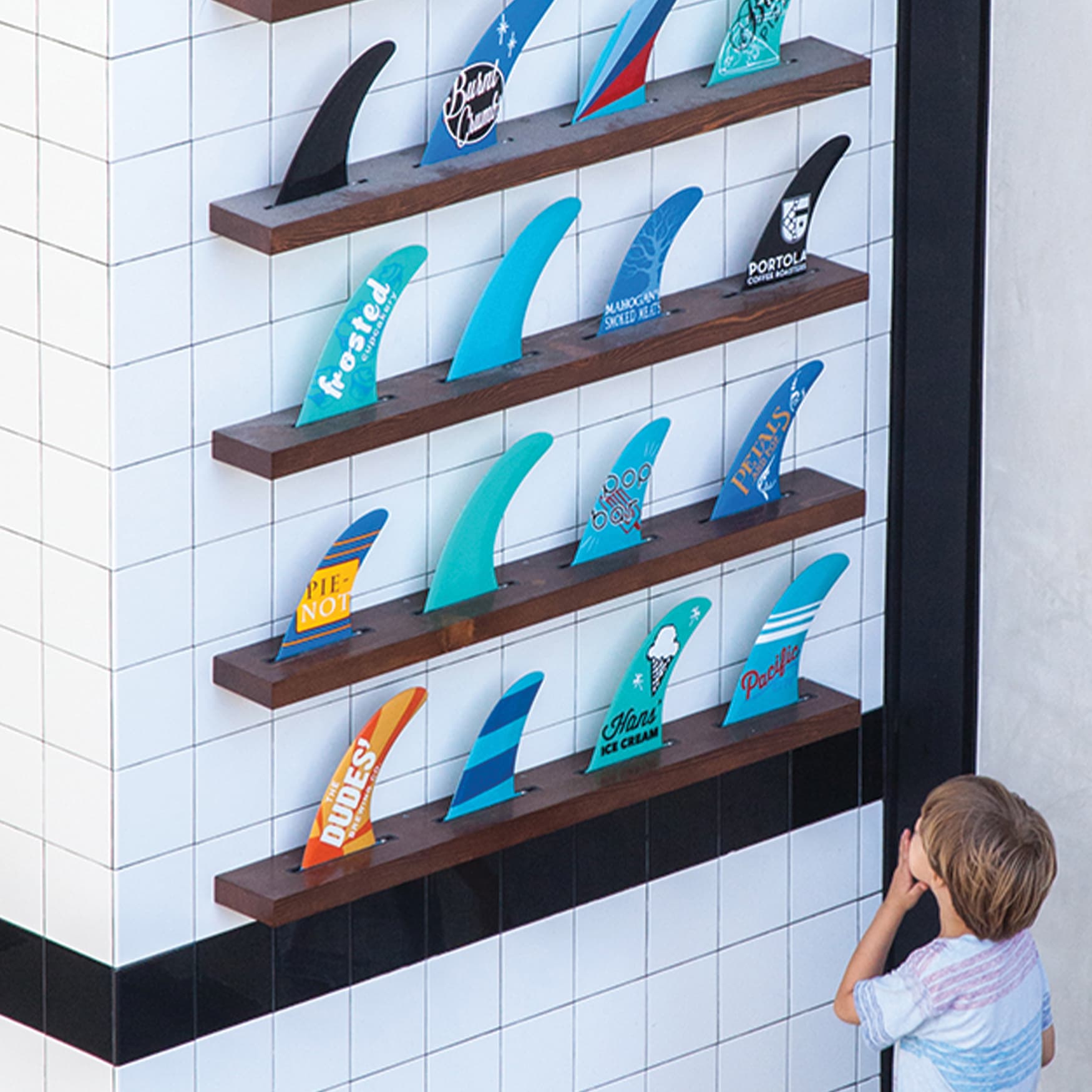 Pacific City specialty graphic installation of surf fins lined up on a wall covered in art and project information.