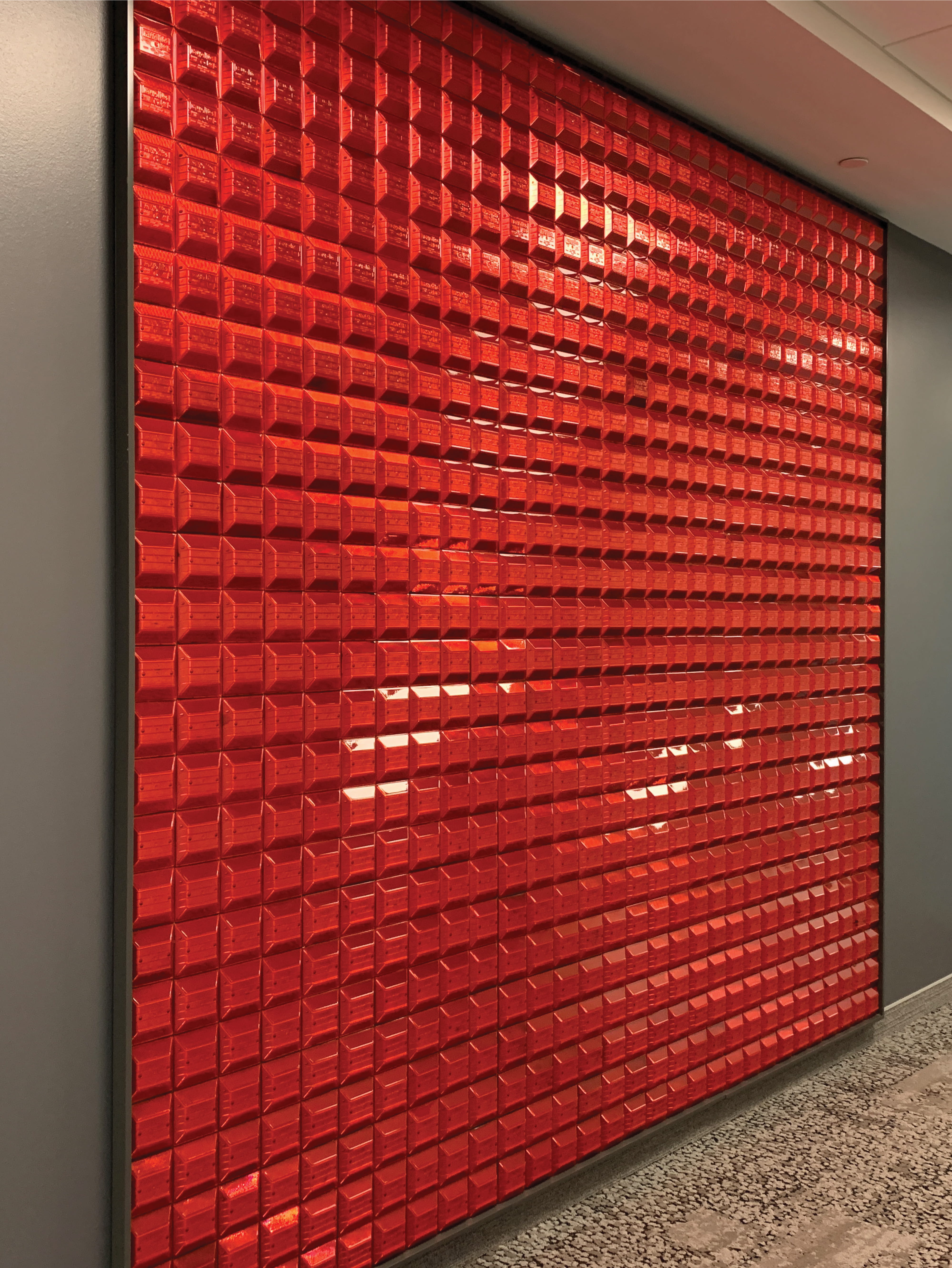 Wall composed of modular red acrylic vehicle lights, creating an immersive environmental graphic design feature that blends experiential design, brand storytelling, and placemaking within a corporate and media workplace environment.