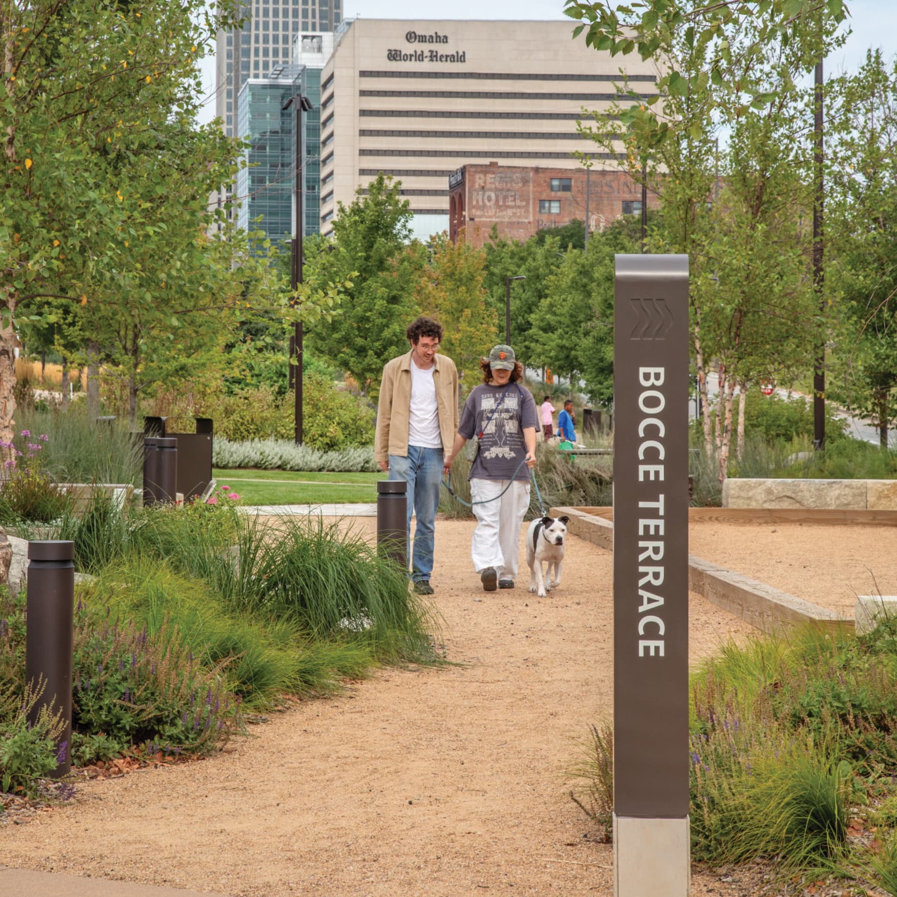 Image of two people walking a dog at the Omaha RiverFront in Omaha, Nebraska. Bocce Terrace directional sign at Omaha Park designed by RSM Design. 