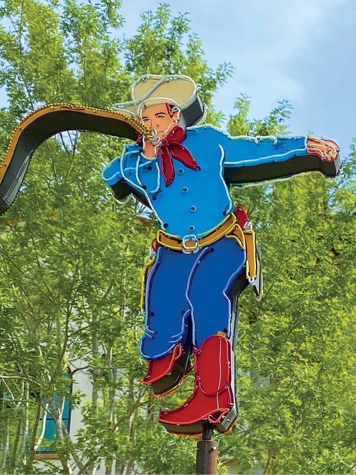 Vintage neon cowboy sign at Hotel Drover in Fort Worth Stockyards, Texas, depicting a colorful Western figure in a blue shirt, red bandana, cowboy hat, and red boots swinging a lasso
