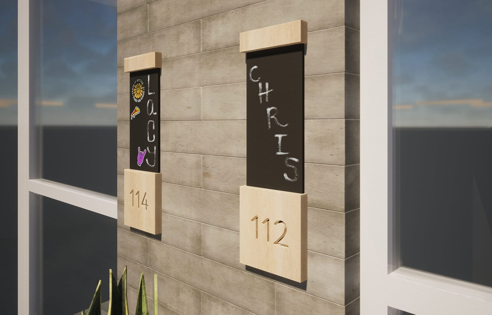Rendering of two resident door signs at Bloc House, mounted on a concrete tile corridor wall. Each sign features a light wood frame with a chalkboard panel for personalization and an engraved unit number below. Unit 114 displays the name "Lacy" written vertically with stickers, while unit 112 shows "Chris" written in chalk, illustrating how residents can customize their entryways.