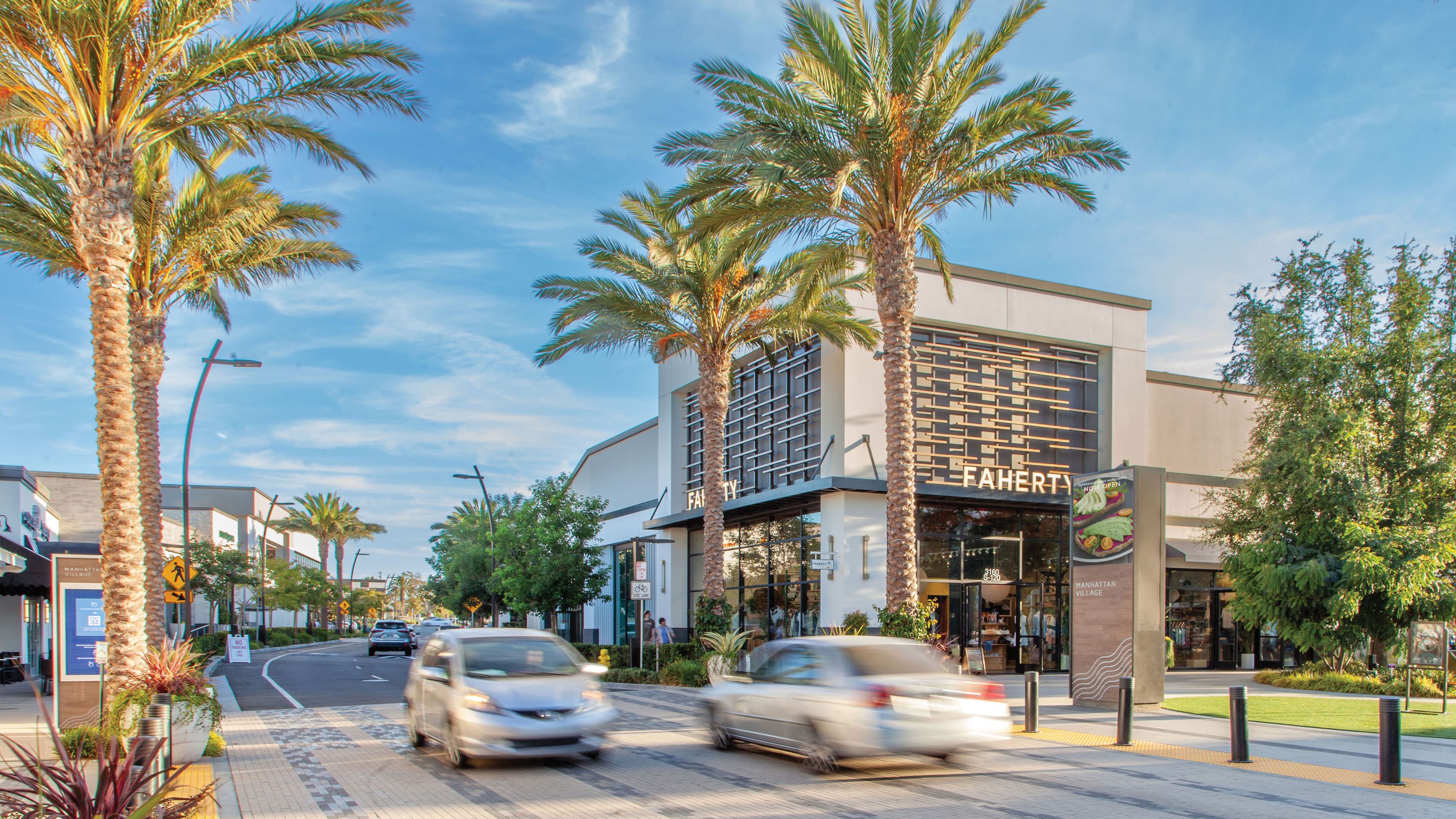 A view of the retail center entry at Manhattan Village with palm trees and cars in the background.