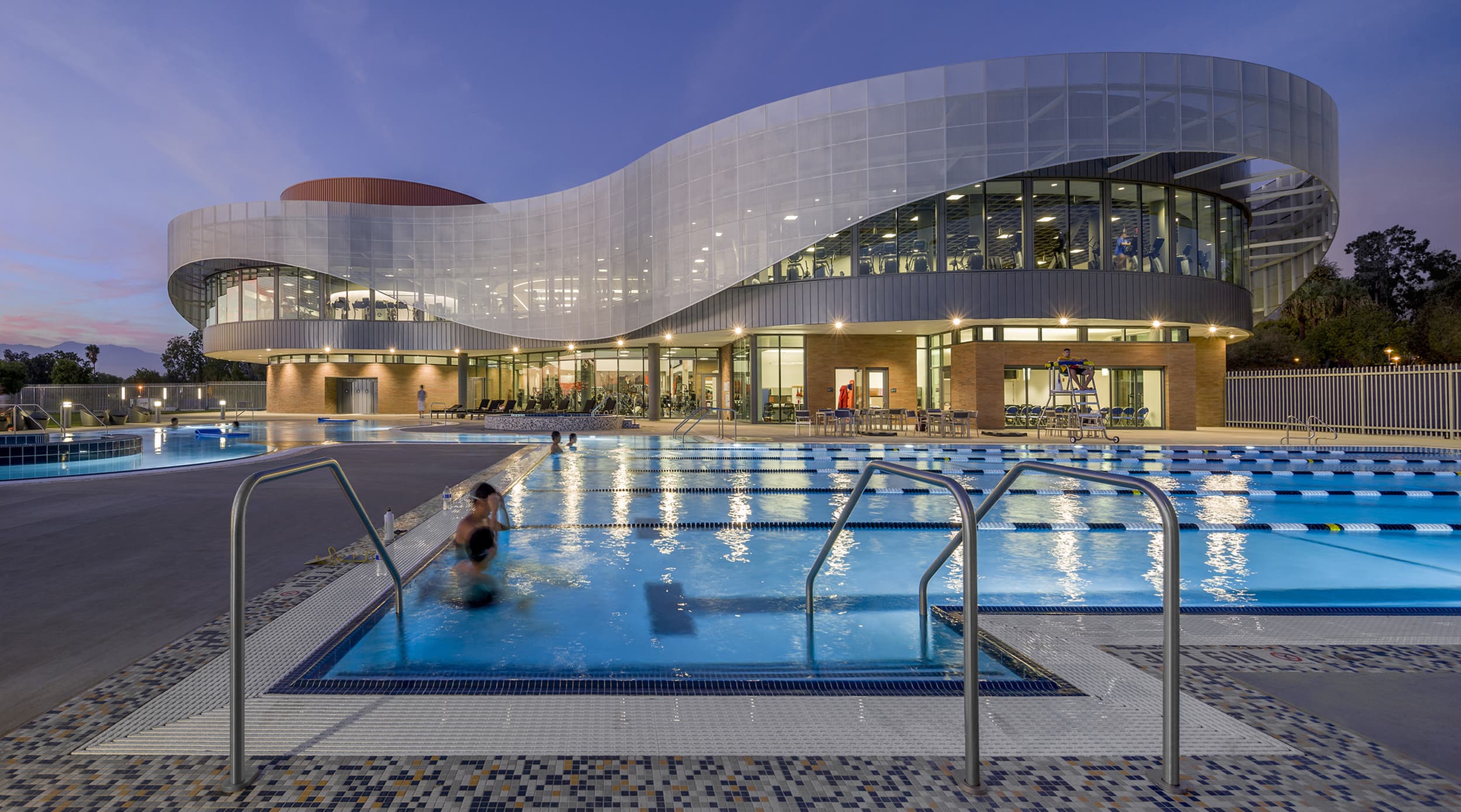 People swimming in an outdoor pool at night at a college recreation center