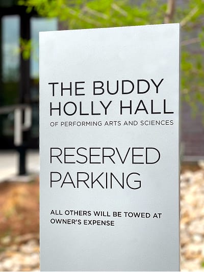 Exterior reserved parking sign for The Buddy Holly Hall of Performing Arts and Sciences featuring clean modern typography on a light gray panel, Lubbock Texas