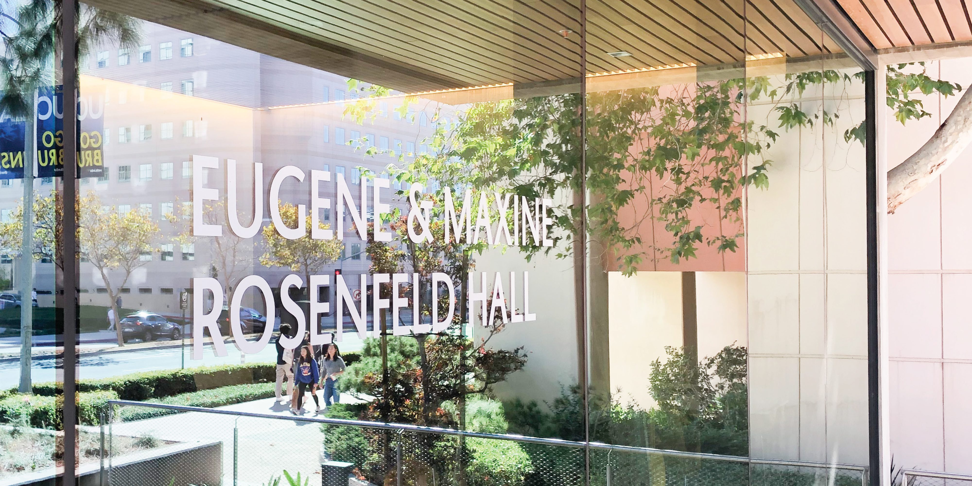 Environmental graphic design and architectural signage for Eugene & Maxine Rosenfeld Hall featuring large-scale glass building identification that enhances campus wayfinding, placemaking, and experiential design within a higher education environment.
