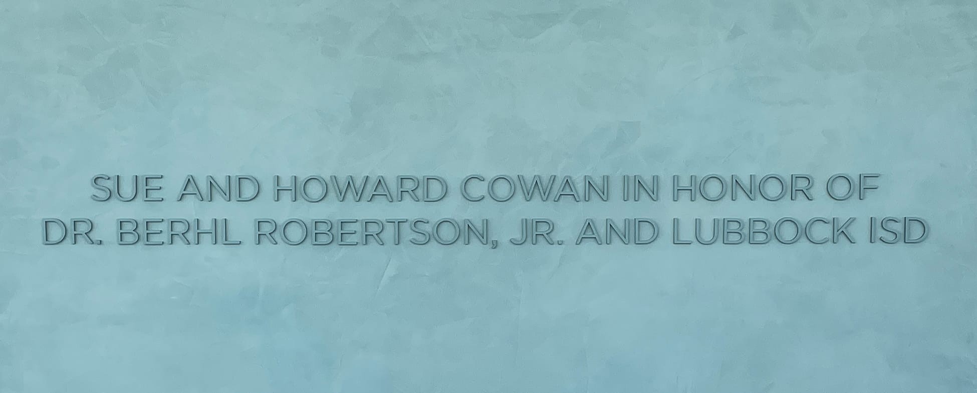 Embossed donor recognition wall inscription reading 'Sue and Howard Cowan in Honor of Dr. Berhl Robertson, Jr. and Lubbock ISD' on a textured teal surface at the Buddy Holly Hall of Performing Arts and Sciences, Lubbock Texas