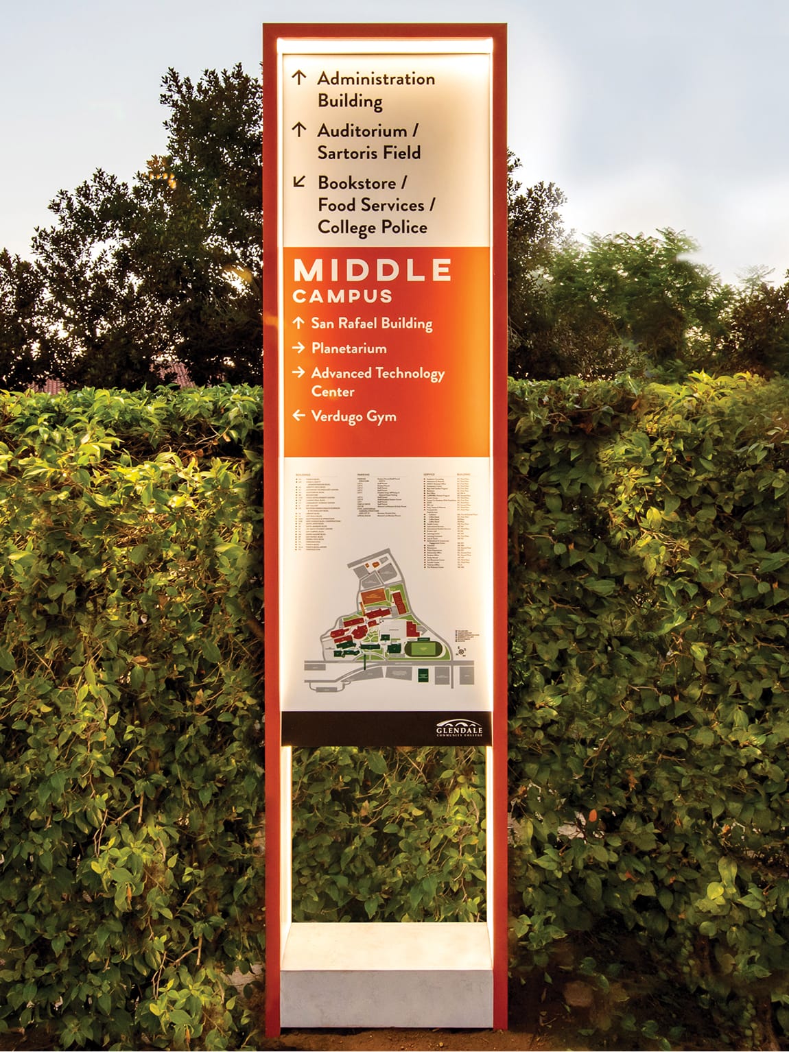 Illuminated campus directory pylon for Glendale Community College Middle Campus designed by RSM Design, featuring directional listings, campus map, and orange branded frame against a green hedge backdrop
