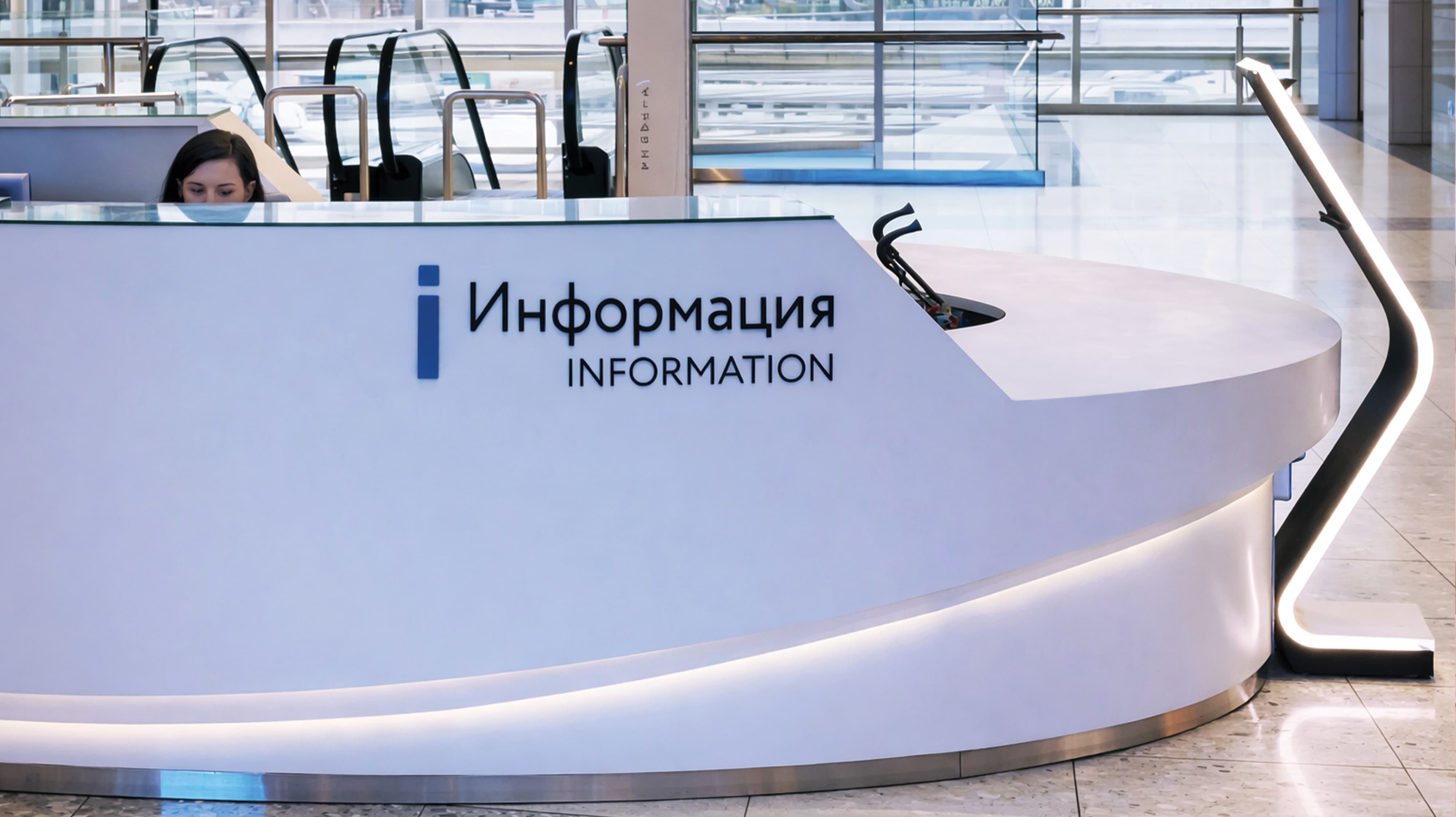 Bilingual Russian and English information desk with branded identification signage in a large-scale international retail or mixed-use destination — RSM Design wayfinding and signage design, master sign programs, environmental graphic design, and international placemaking for retail, mixed-use, transit, and international destinations.
