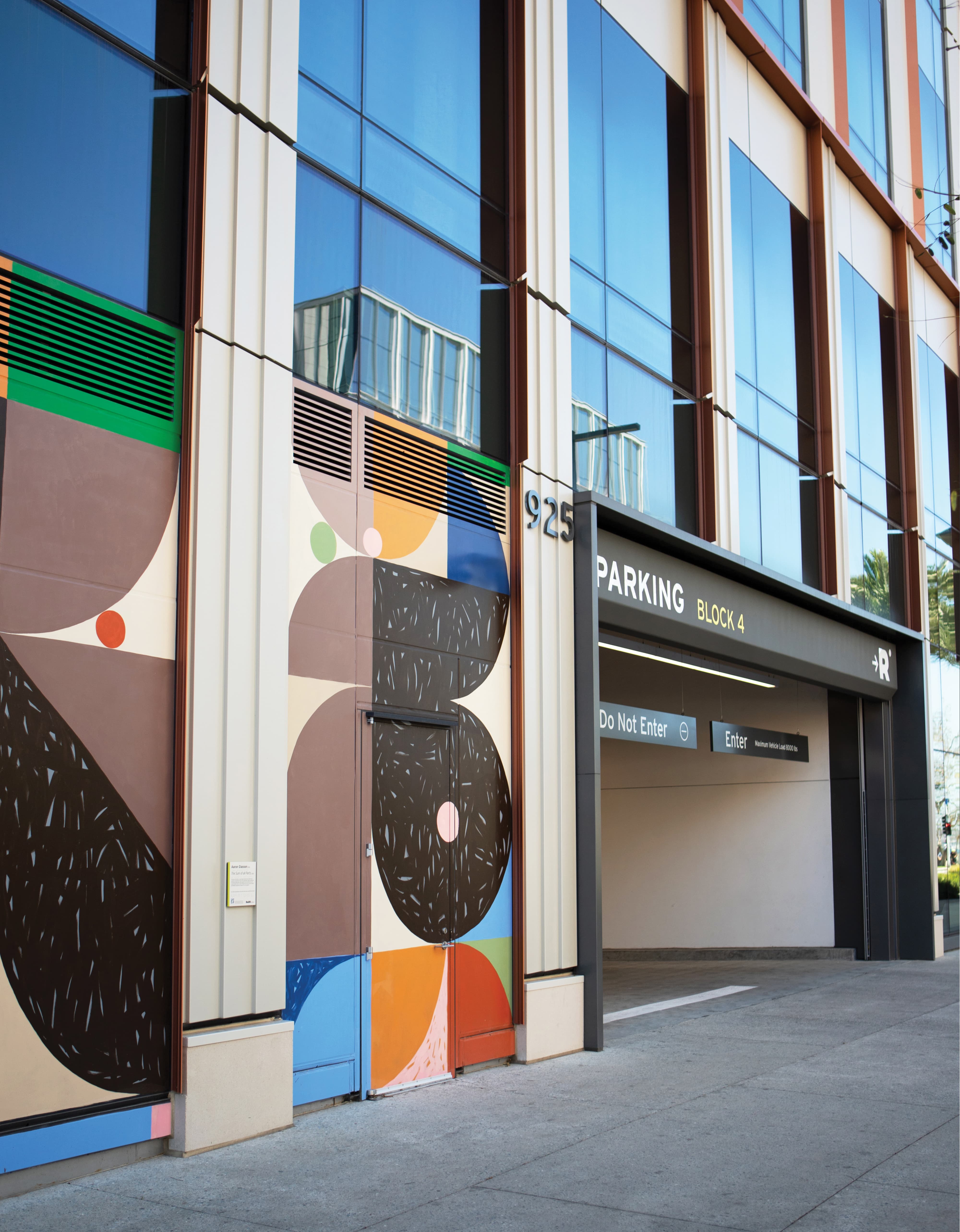 Building exterior at 925 featuring a colorful geometric mural of circles and shapes in brown, orange, blue, and green beside a parking garage entrance sign reading 'Parking Block 4, Do Not Enter, Enter,' with the RαDD arrow logo overhead.