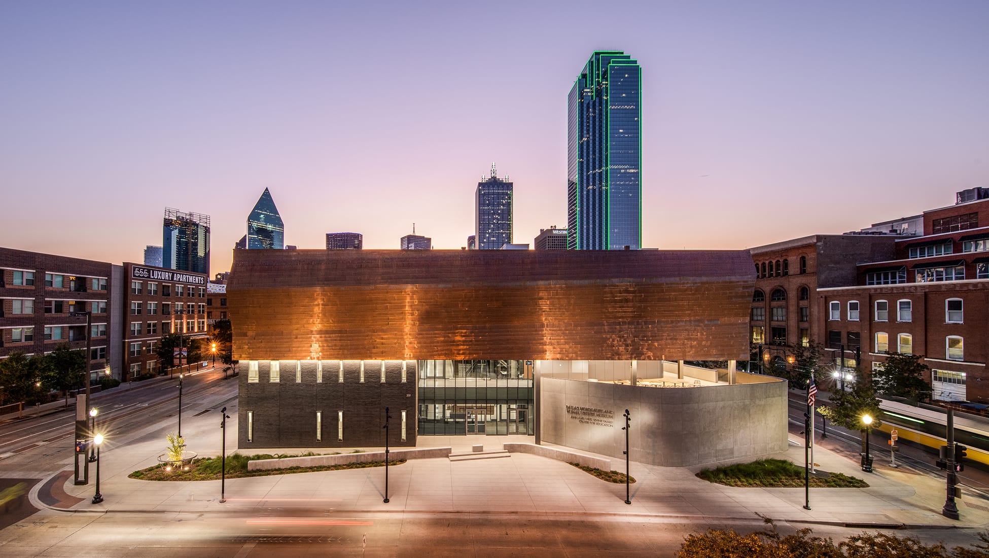 Dallas Holocaust and Human Rights Museum exterior at dusk with Dallas skyline backdrop - environmental graphic design and wayfinding by RSM Design
