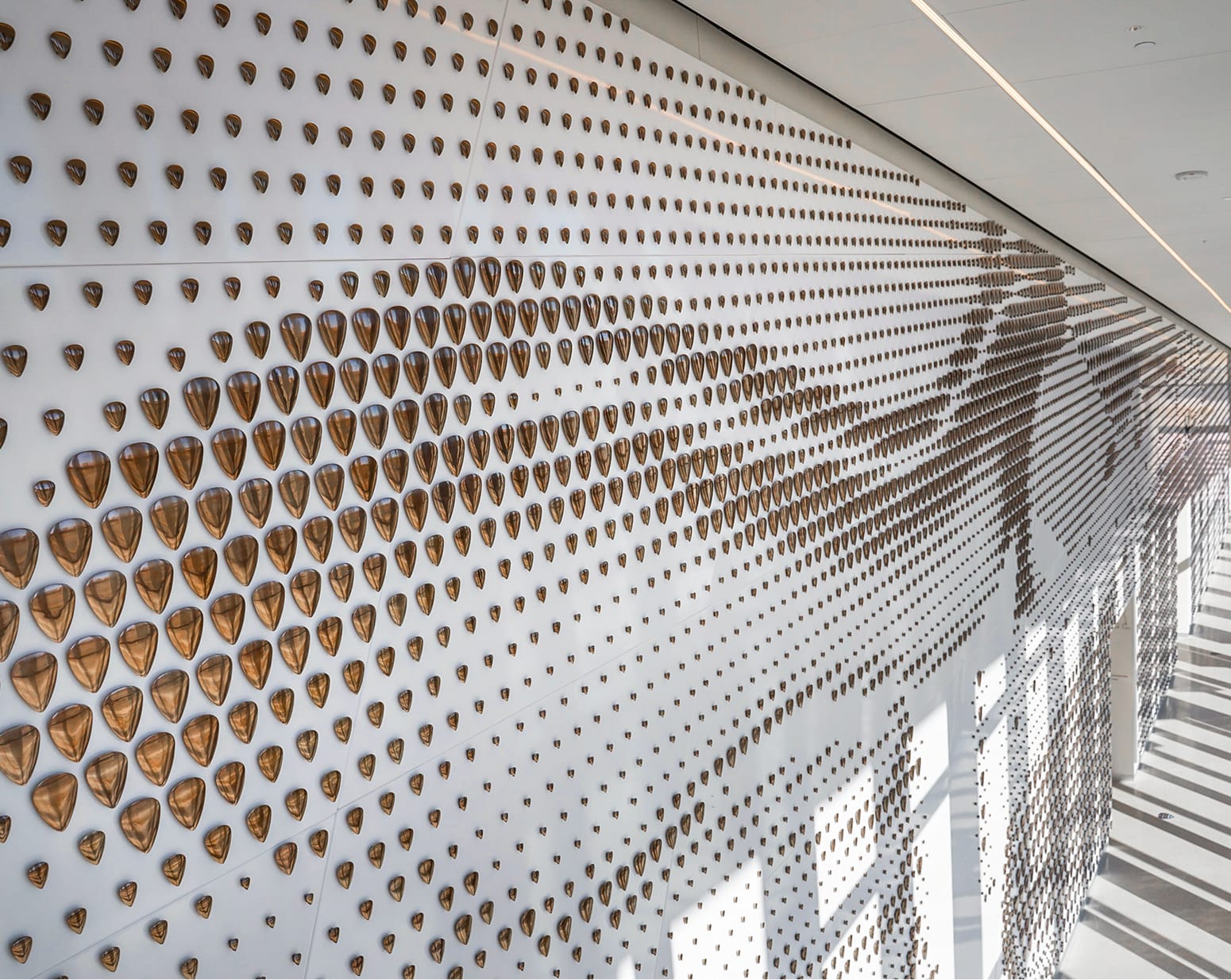 Large-scale interior art installation featuring thousands of bronze guitar picks arranged in a dynamic wave pattern on a white wall, paying tribute to Buddy Holly at the Lubbock Independent School District administrative building, Lubbock Texas