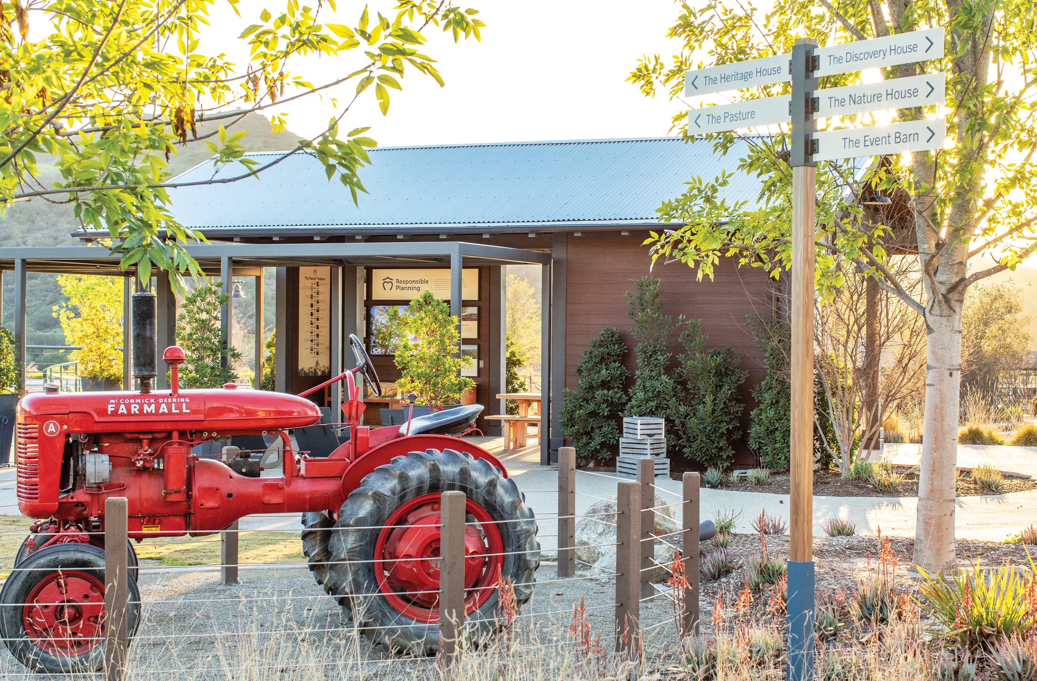Image of tractor at Ranch Camp at Rancho Mission Viejo with directional flag sign in a clean, modern sign and typeface. Modern barn is seen in the background with Responsible Planning. ,