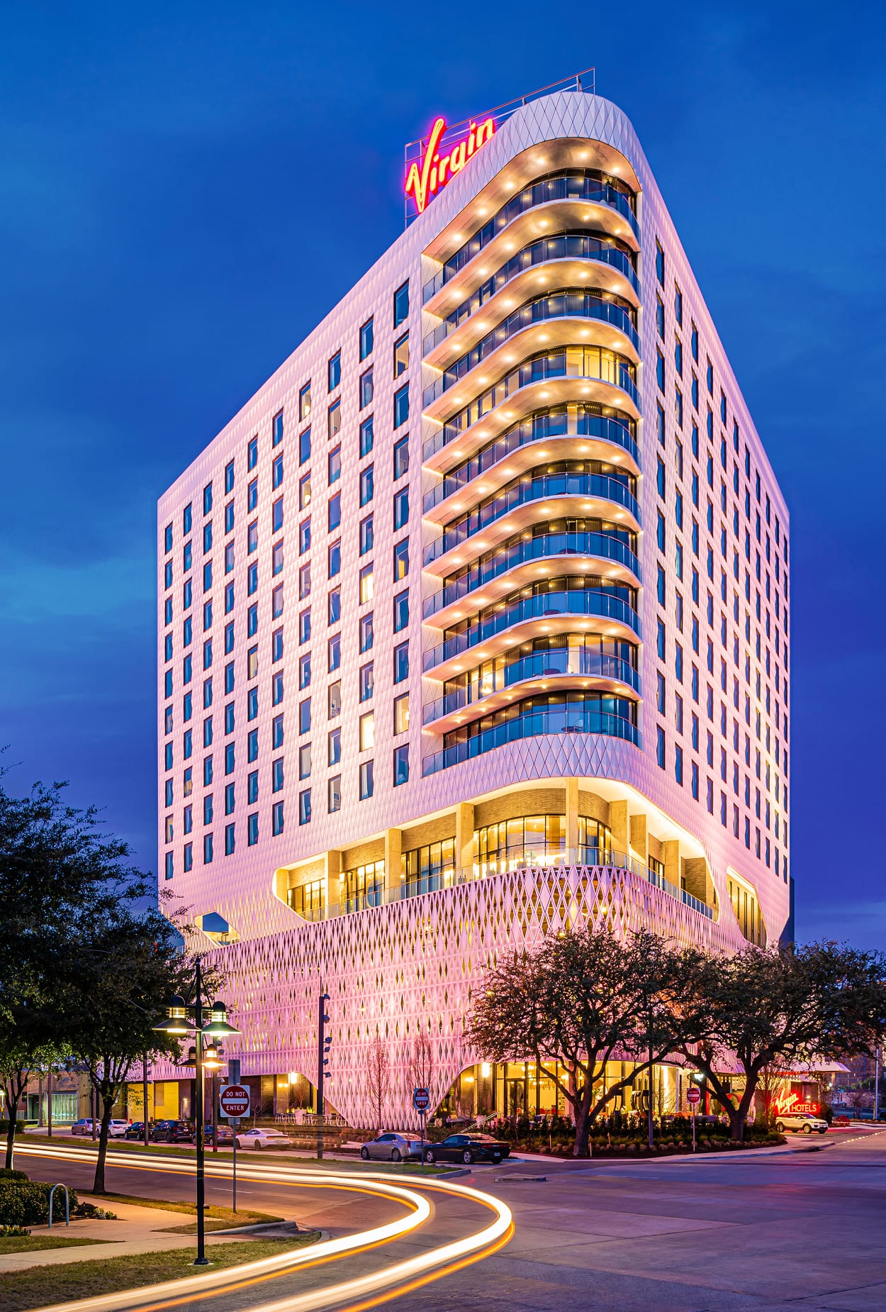 Virgin Hotels Dallas exterior at dusk featuring rooftop neon sign and illuminated facade - large-scale architectural signage and environmental branding design by RSM Design, a leading wayfinding and signage design firm