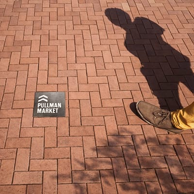 Branded ground wayfinding marker for Pullman Market embedded in brick paving at San Antonio’s Pearl District, guiding pedestrians through the walkable urban streetscape.