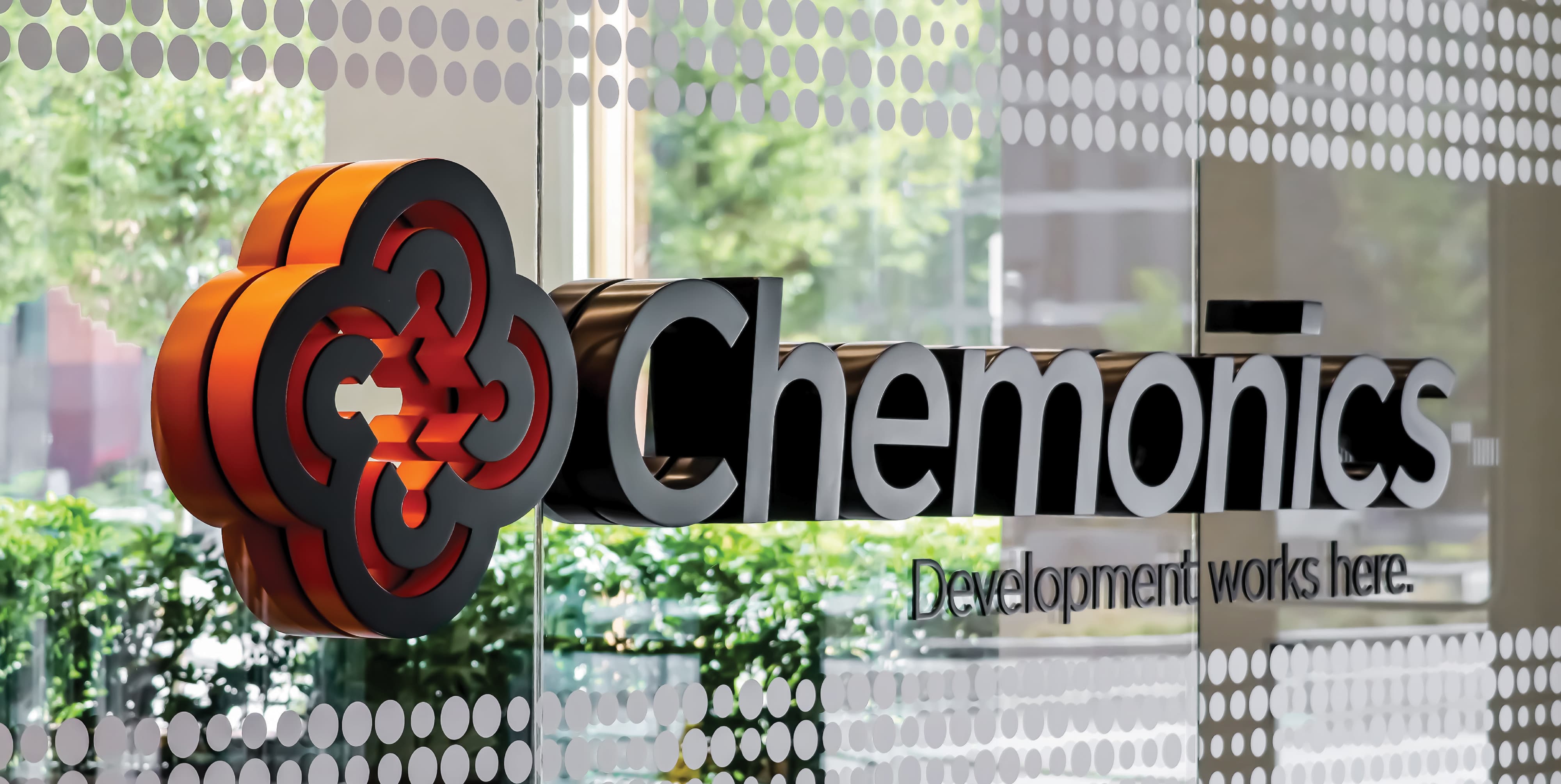 Dimensional Chemonics brand logo and interior signage applied to glass, featuring integrated lighting and environmental graphics, highlighting brand strategy, experiential design, and workplace wayfinding for corporate and innovation environments.