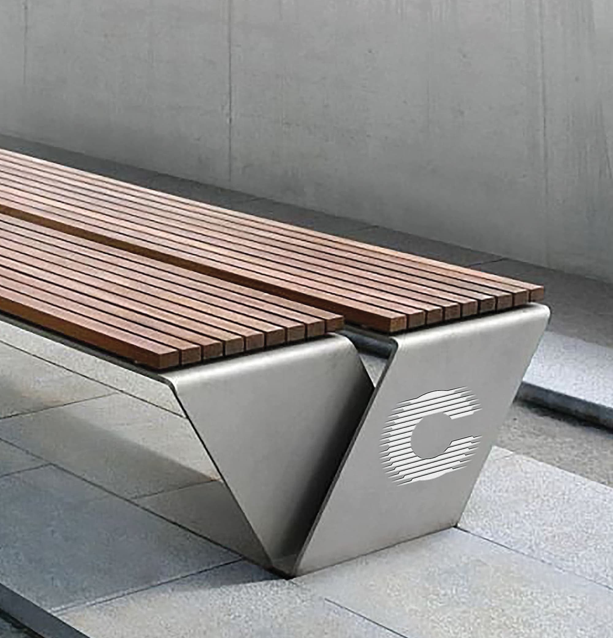 A sleek transit station bench featuring warm wood slat seating supported by angular brushed stainless steel legs with the Cucamonga Station "C" logomark etched into the metal base, set against a concrete wall and paved plaza surface — illustrating RSM Design's branding and visual identity and specialty graphics applied to branded street furniture and placemaking within the transit and streetscape markets