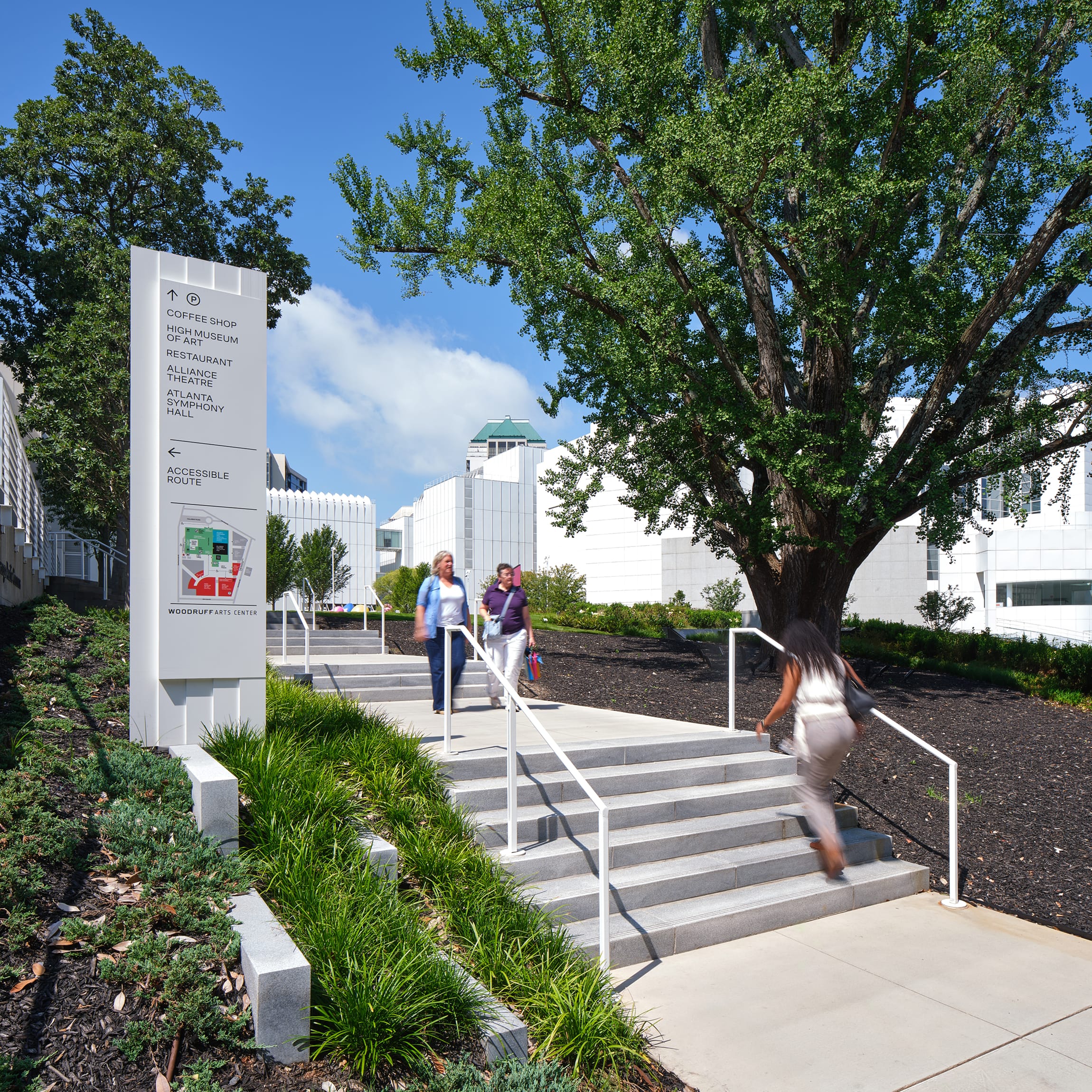 Pedestrian directional sign with campus map, directory listings, and accessible route arrow beside outdoor steps leading toward the High Museum of Art, Alliance Theatre, and Atlanta Symphony Hall at the Woodruff Arts Center – campus wayfinding and environmental graphic design by RSM Design.