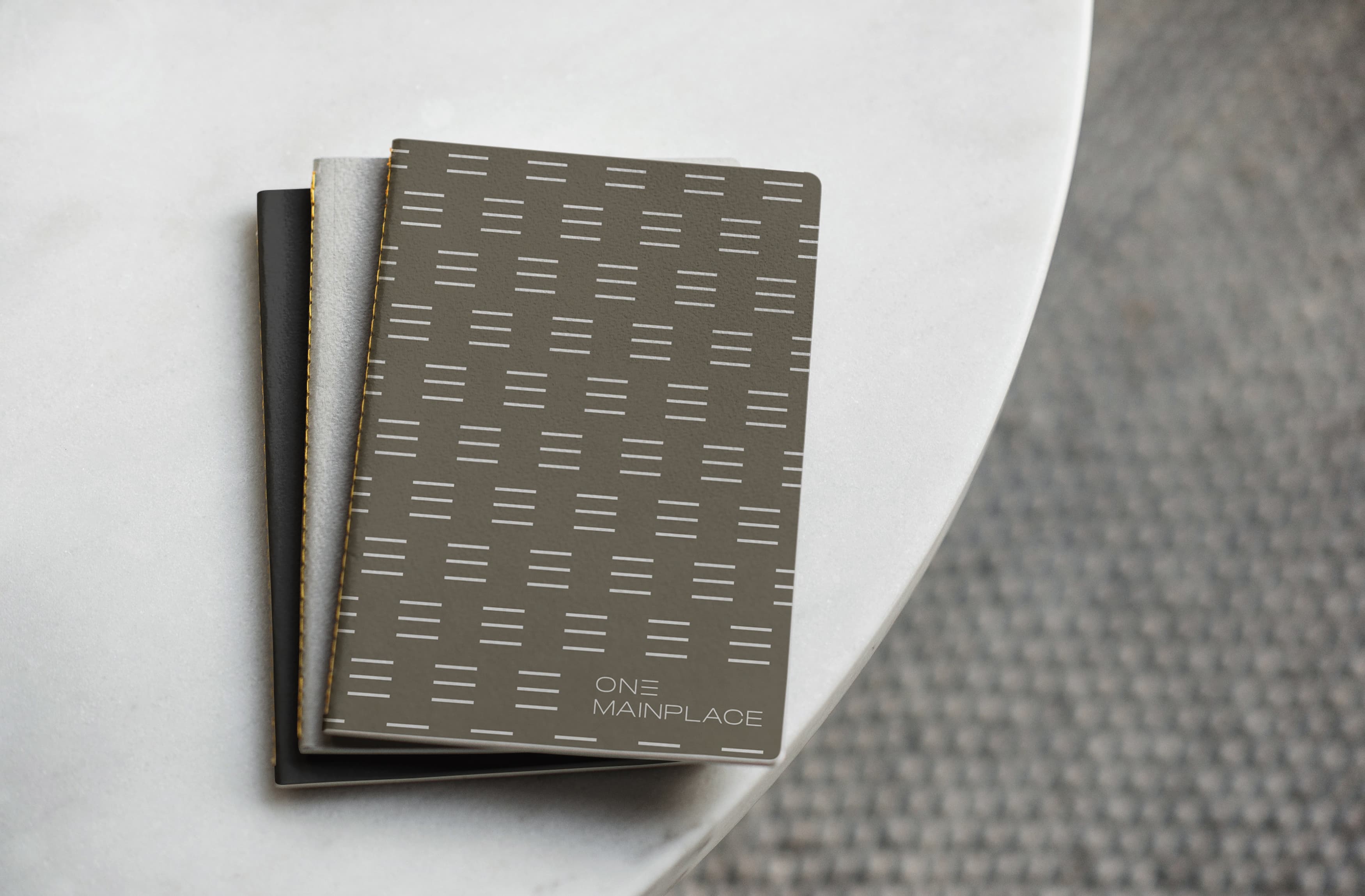 Notebooks for the workplace building with branded patterning and One MainPlace logo mark in bottom right corner