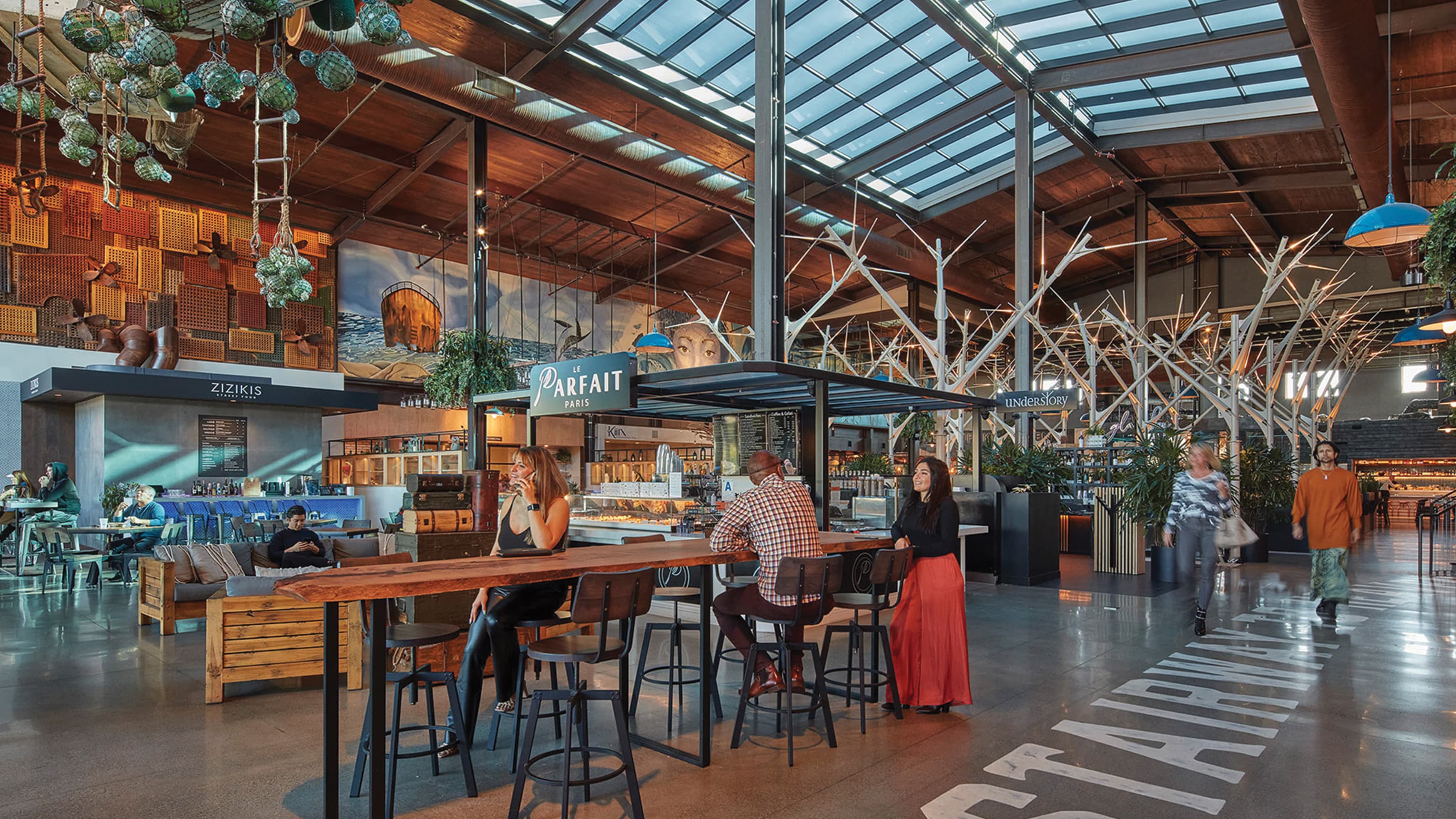 Eclectic food hall with large skylight window, exposed wood ceiling, tables, and sculptural elements for as creative placemaking design