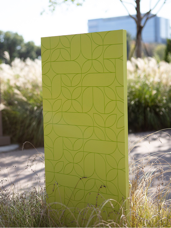 Lime green freestanding wayfinding monolith with engraved geometric pattern design surrounded by ornamental grasses at Kaleidoscope Park, Frisco, Texas