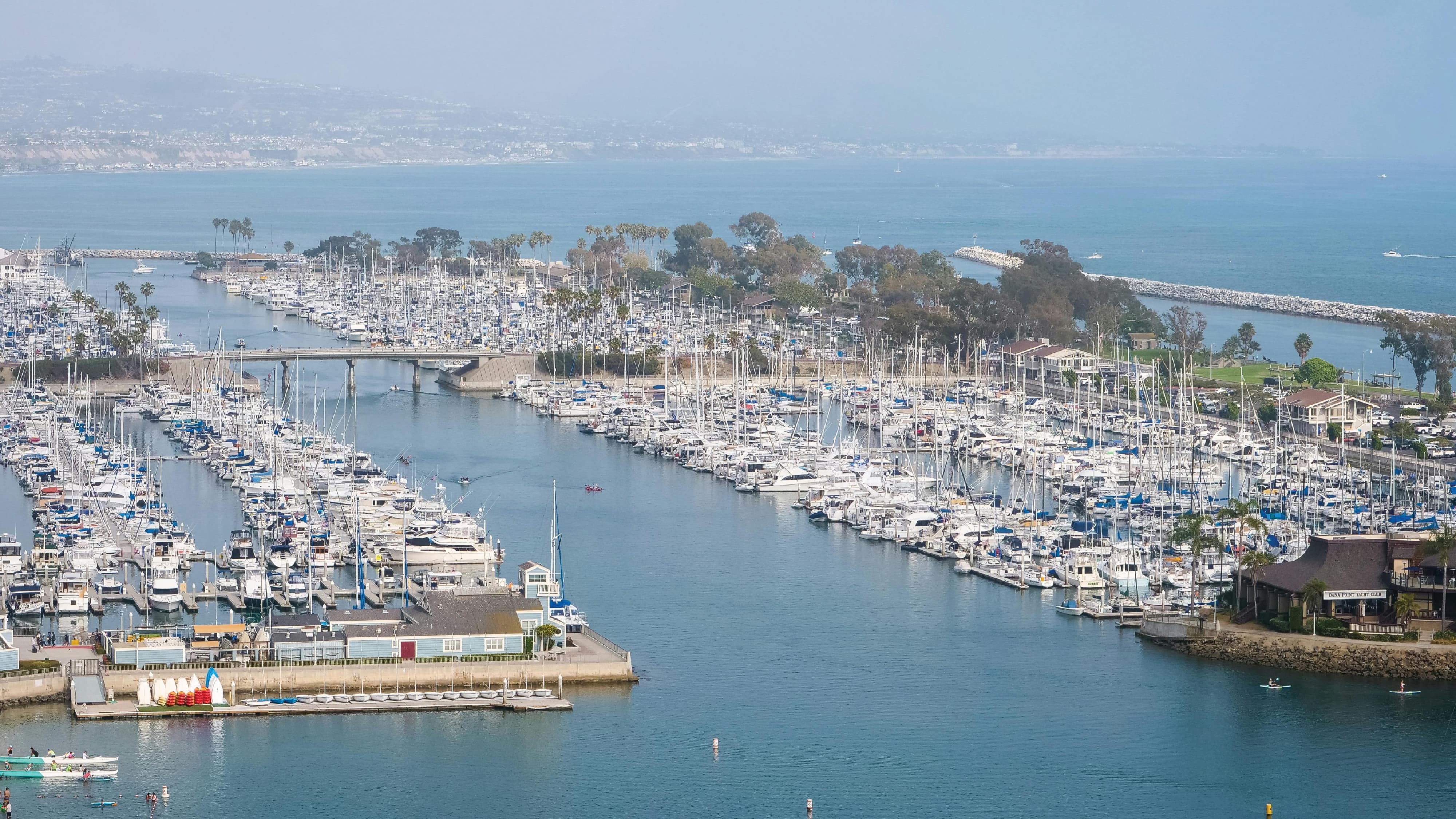 Aerial view of Dana Point Harbor waterfront marina with hundreds of sailboats and yachts docked along channels leading to the Pacific Ocean in Dana Point, California — RSM Design environmental graphic design, wayfinding and signage design, experiential placemaking, and branded environments for waterfront, civic, park, and mixed-use destinations.