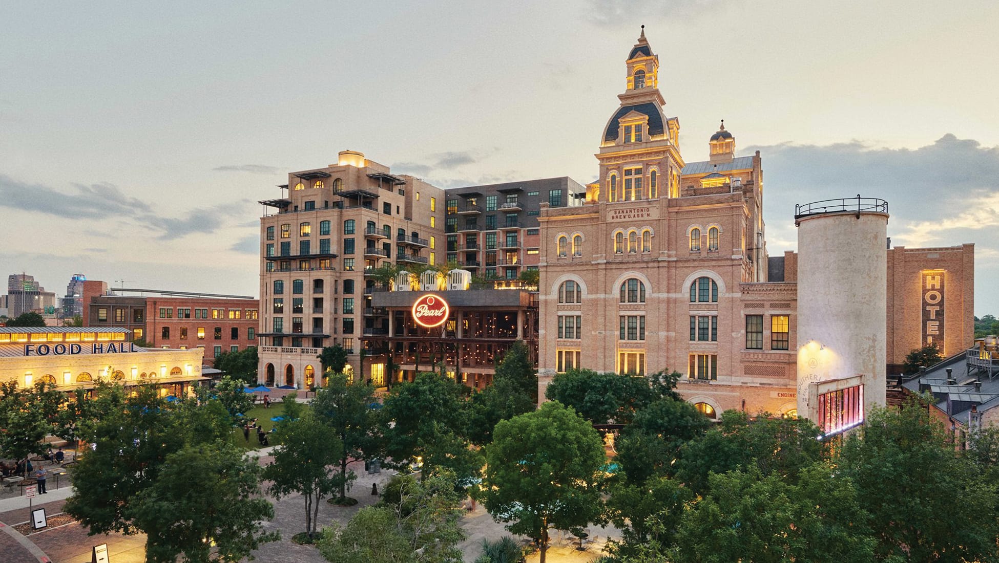 San Antonio Pearl District at dusk featuring historic brewery architecture, modern mixed-use buildings, illuminated signage, food hall, and landscaped public plaza showcasing urban redevelopment and placemaking design by RSM Design.