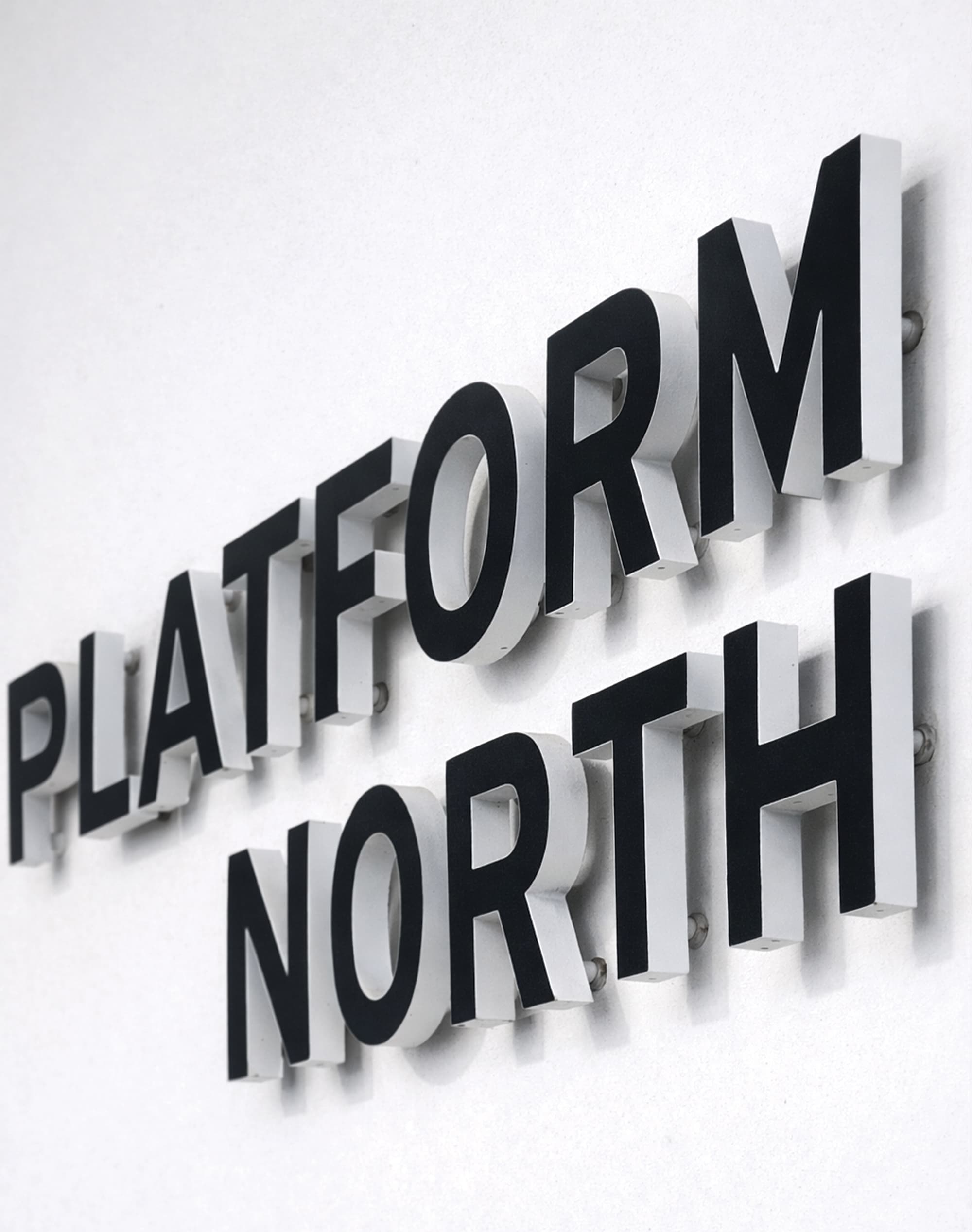 Close-up of dimensional black and white "Platform North" channel letters mounted on a white exterior wall, showcasing building identification and signage design for a mixed-use workplace environment by RSM Design.