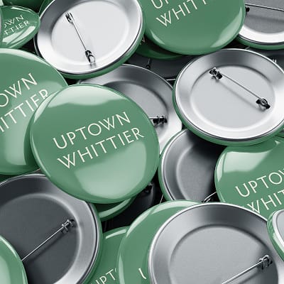 Uptown Whittier branded pins featuring clean typography on a green background, extending the district identity into small-scale promotional items.