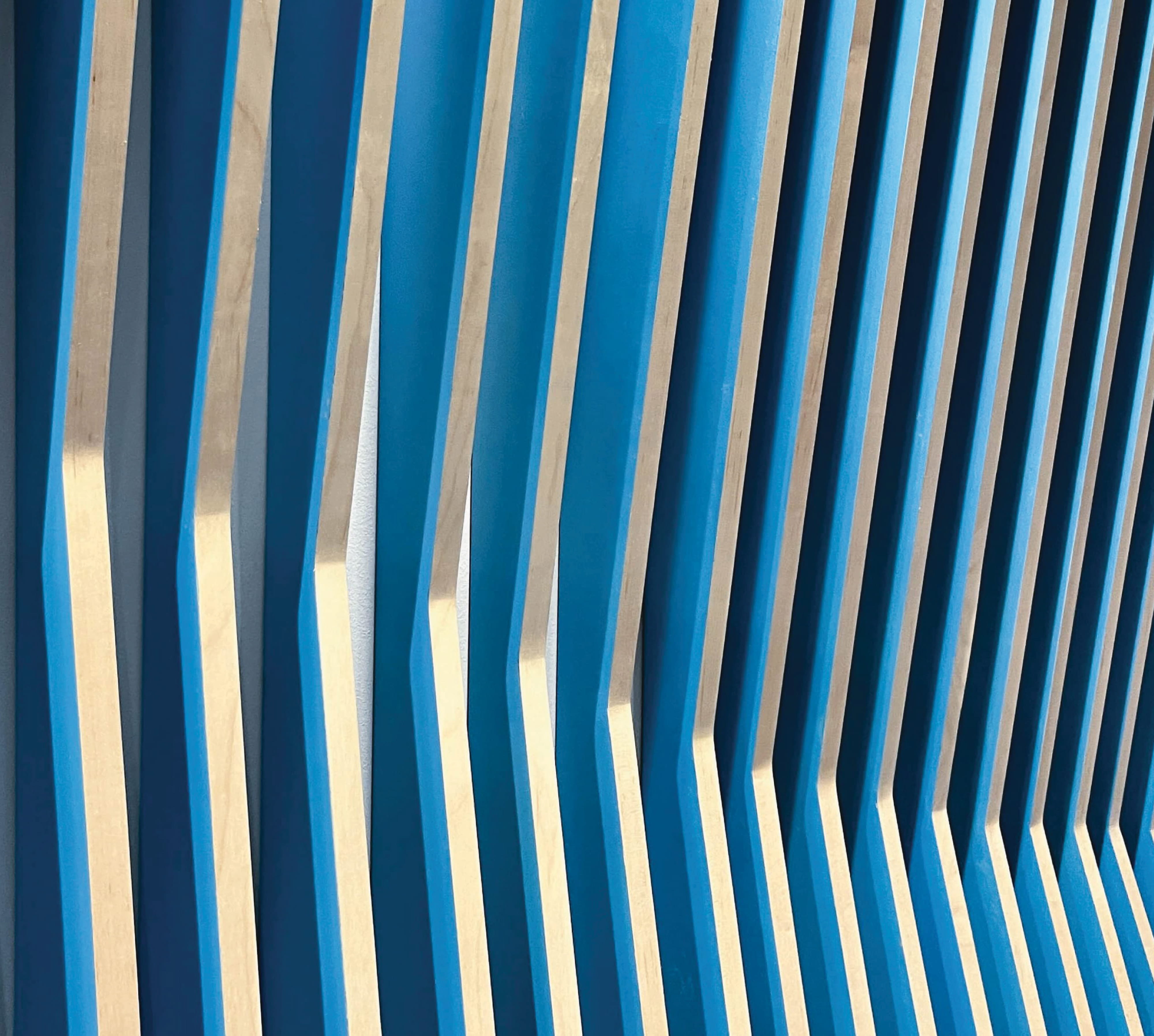 Abstract dimensional wall installation featuring layered blue and wood elements, showcasing environmental graphic design, experiential design, and placemaking through material expression within a corporate workplace and branded interior environment.