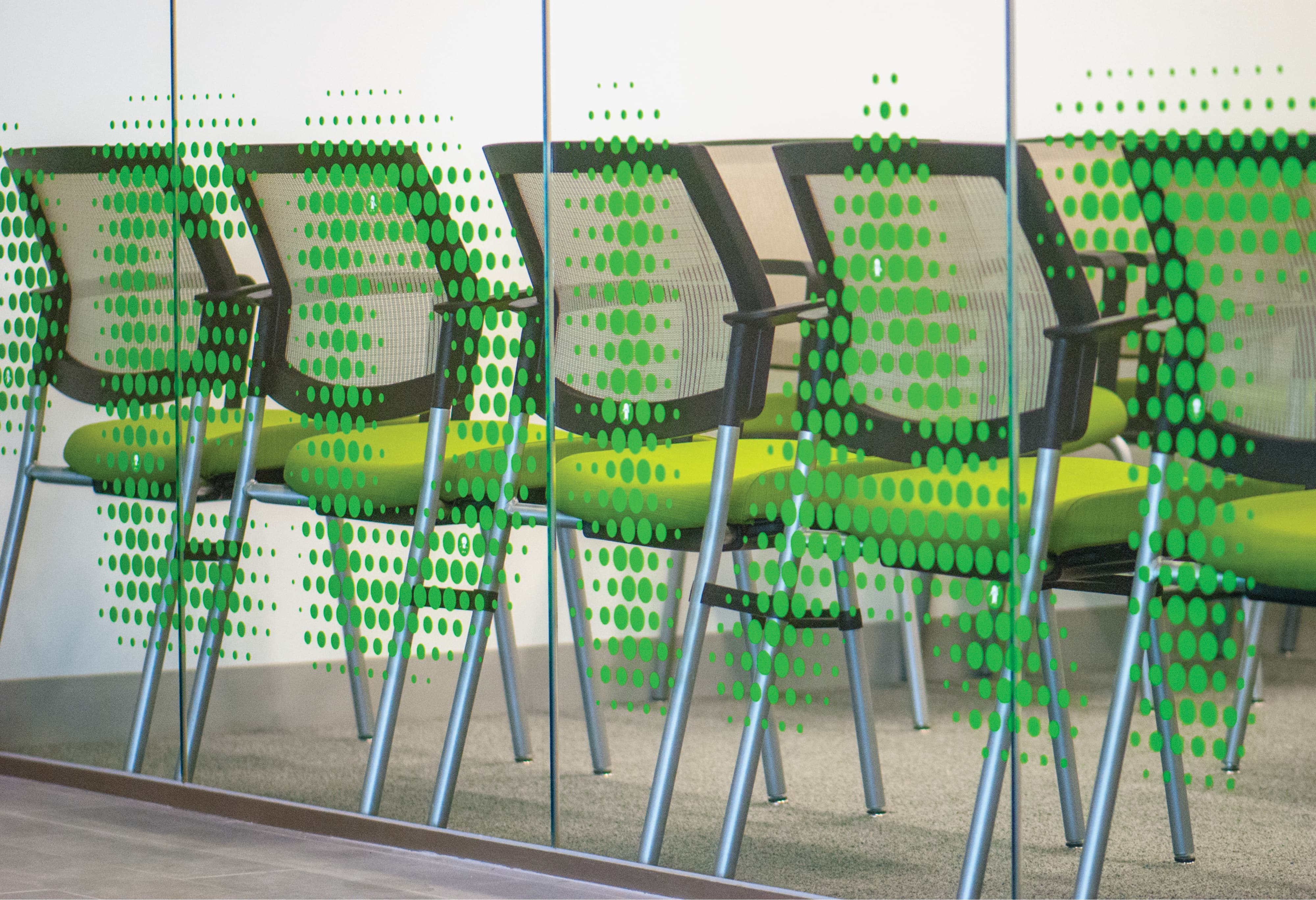 Interior waiting area viewed through a gradient green dot-pattern glass graphic on a glazed partition wall at University of the Pacific San Francisco Campus dental clinic, with green upholstered seating chairs visible through the layered experiential graphic — RSM Design specialty graphics, experiential graphics, branded environments, and environmental graphic design for education and health and wellness destinations.