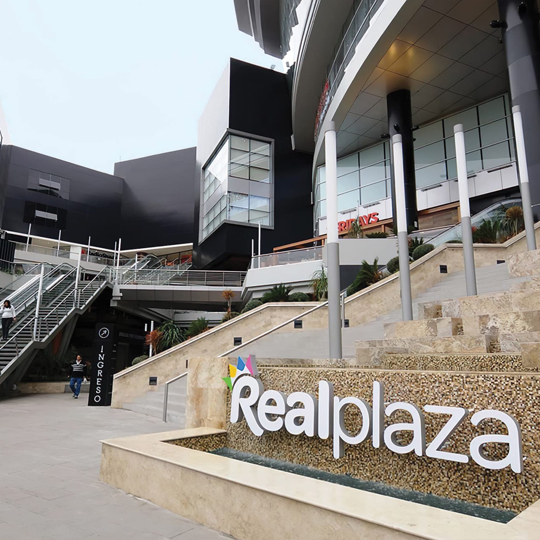 Exterior entrance of Real Plaza Salaverry shopping mall in Lima, Peru featuring a prominent white logo sign, outdoor stairs, and modern architectural design.