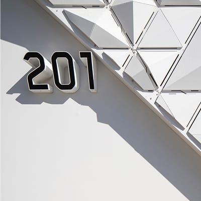 Bold black dimensional address number 201 mounted on white stucco wall beside geometric triangular facade panels casting dramatic shadows
