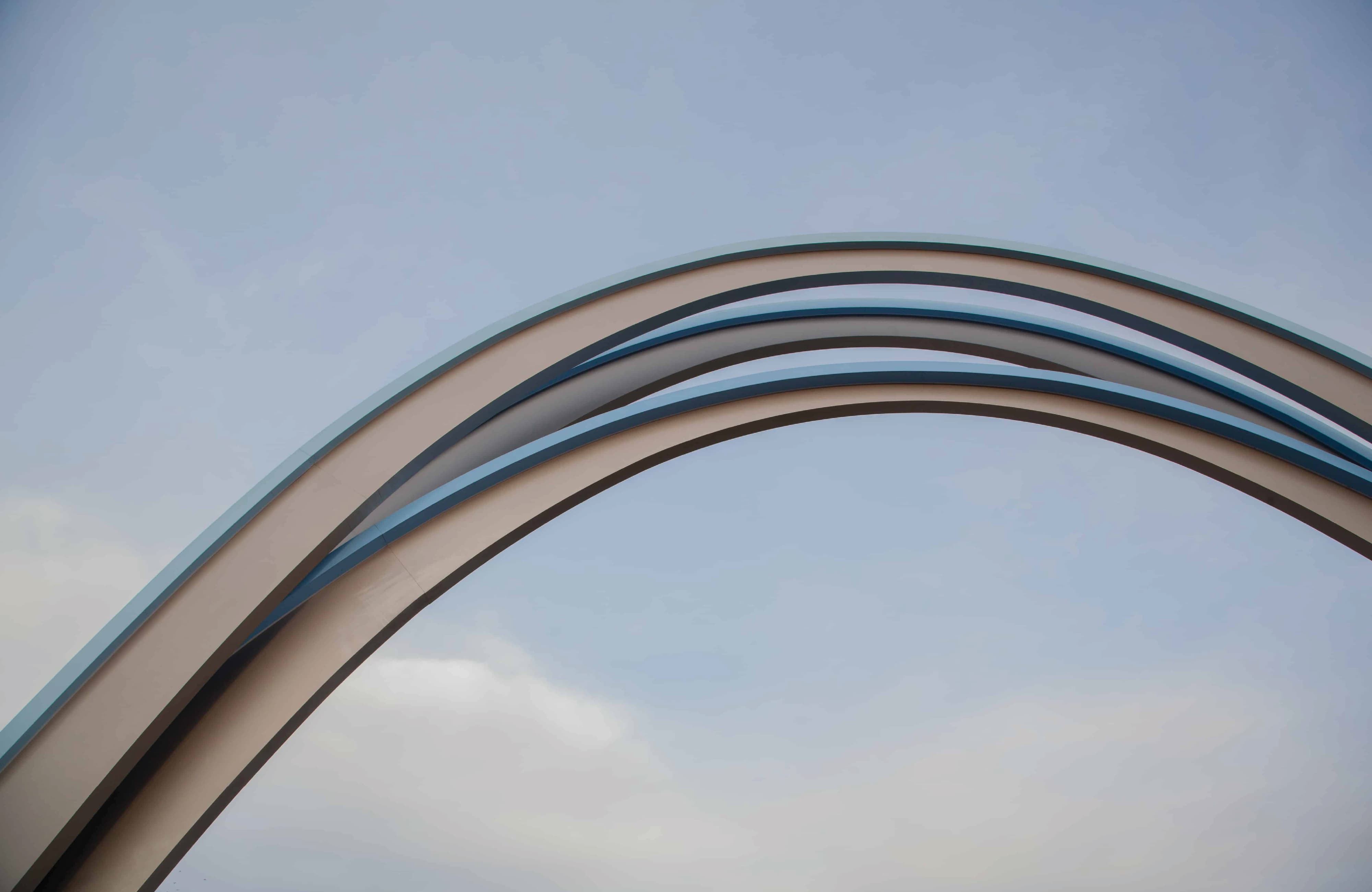 Close-up of two interlocking curved arches in cream and blue against a soft, cloud-streaked sky.