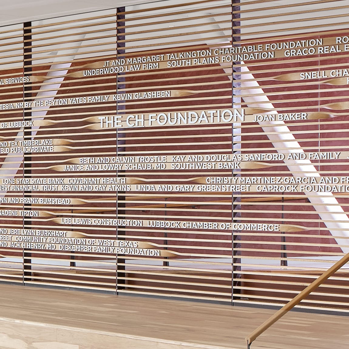 Large-scale donor recognition wall featuring white dimensional lettering on warm wood slat panels listing major contributors including The CH Foundation, Talkington Charitable Foundation, and Lubbock Chamber of Commerce at Buddy Holly Hall of Performing Arts and Sciences, Lubbock Texas