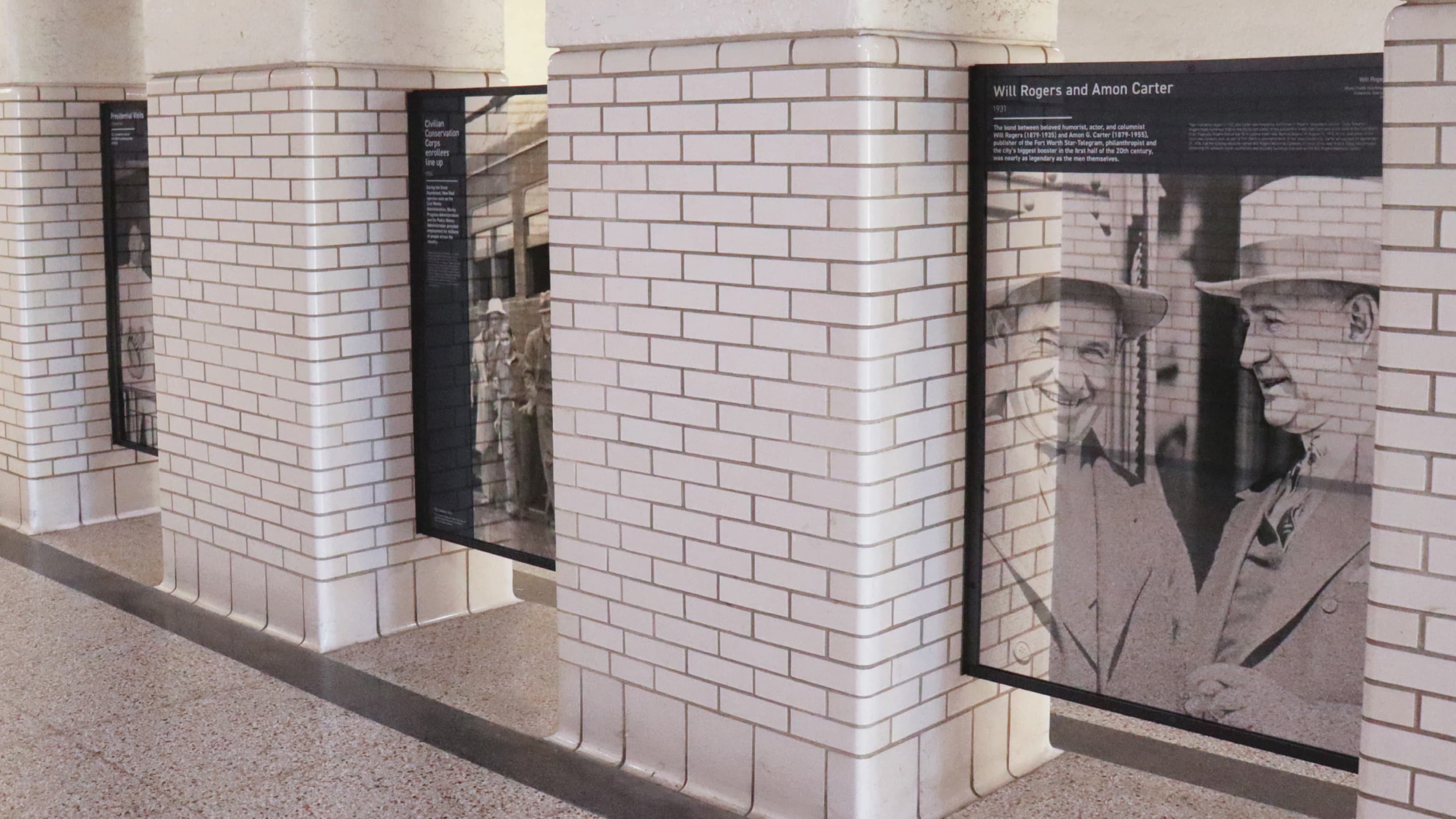 Historic interpretive exhibit panels with large-scale black-and-white archival photographs and narrative text mounted on white brick columns in the T&P Station concourse, showcasing experiential graphics, donor recognition, and cultural placemaking design for a mixed-use transit development by RSM Design.
