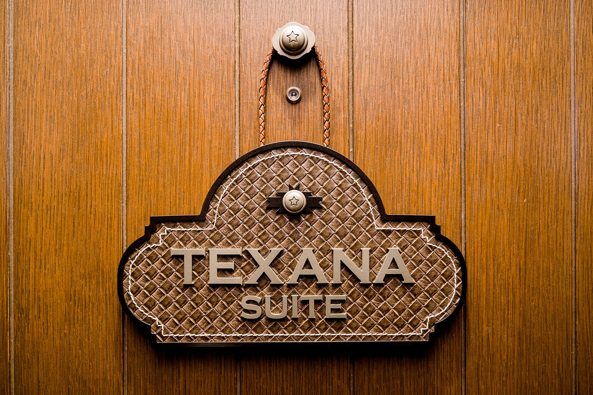 Texana Suite door sign at Hotel Drover, featuring tooled leather detailing, braided leather strap, and Western-style star hardware on a warm wood door in Fort Worth Stockyards, Texas