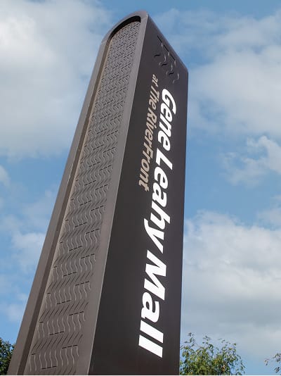 Tall monumental pylon sign for Gene Leahy Mall at the RiverFront in downtown Omaha, Nebraska, featuring textured dark metal construction and bold white typography against a blue sky