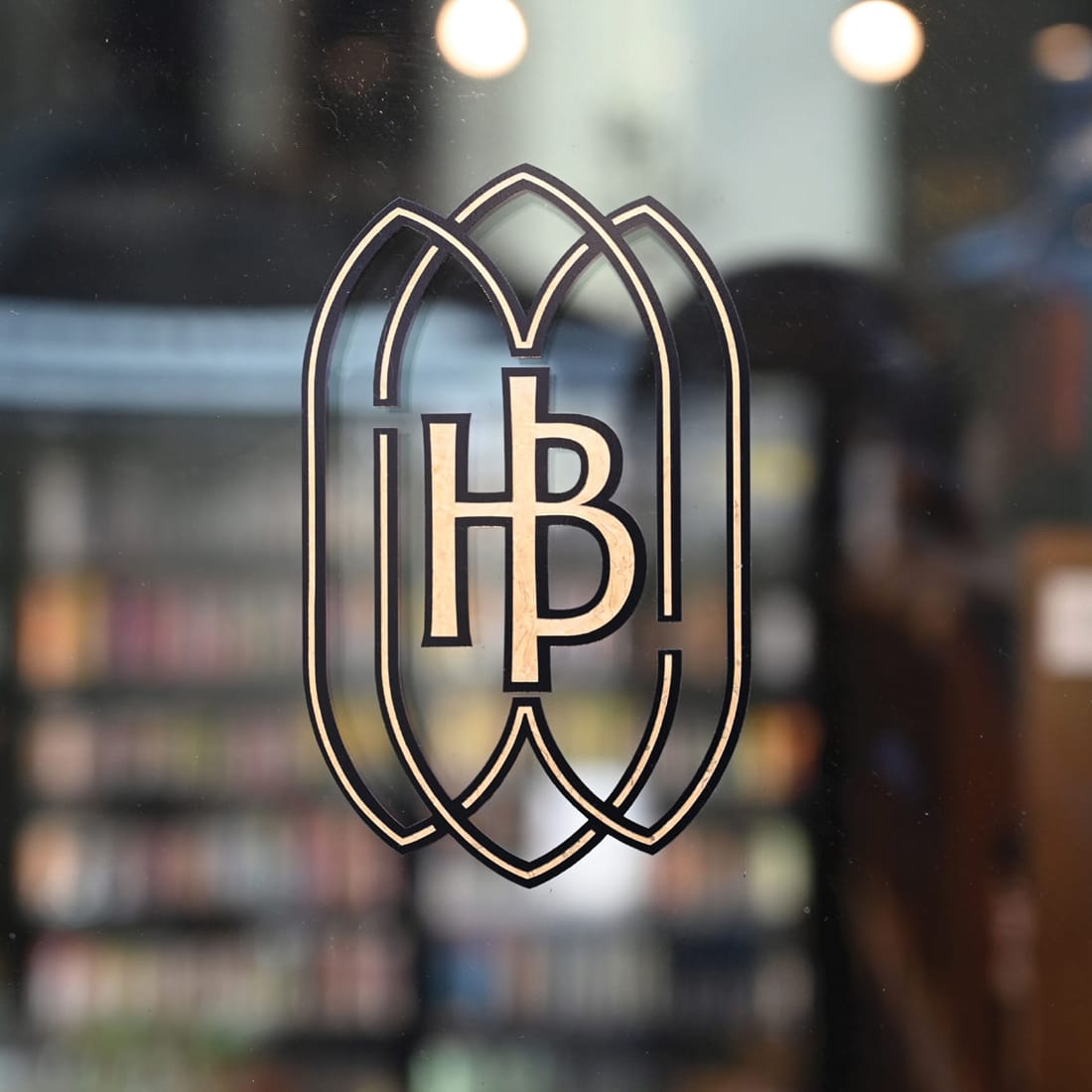 "HB" monogram decal on a storefront glass door with stocked market shelves visible inside — brand identity design by RSM Design