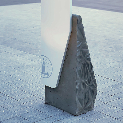 Close-up of custom wayfinding sign base with faceted concrete texture and lighthouse icon, exterior signage detail at San Carlos mixed-use development by RSM Design