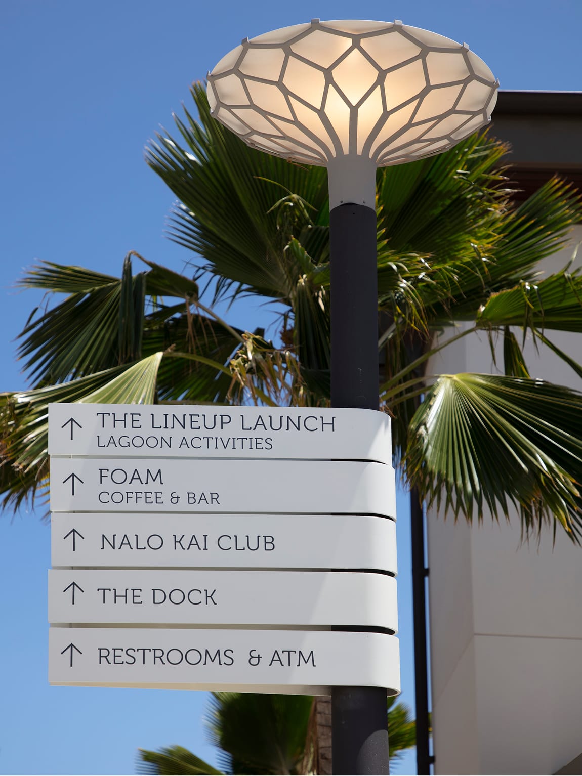 Directional pole sign with stacked panels for The Lineup Launch, Foam, Nalo Kai Club, the dock, and restrooms beneath illuminated lantern light at Wai Kai, Ewa Beach, Oahu, wayfinding by RSM Design.