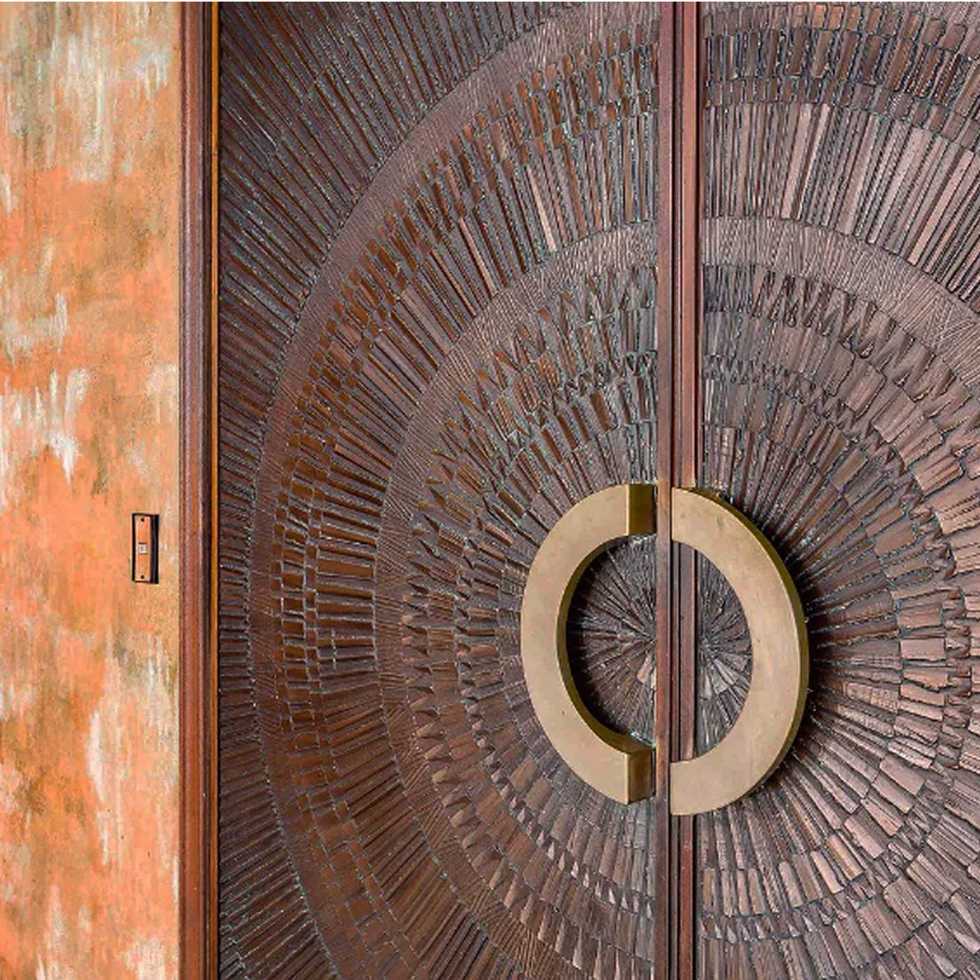 Detail of a carved bronze entry door with a radial sunburst pattern and brass ring handles