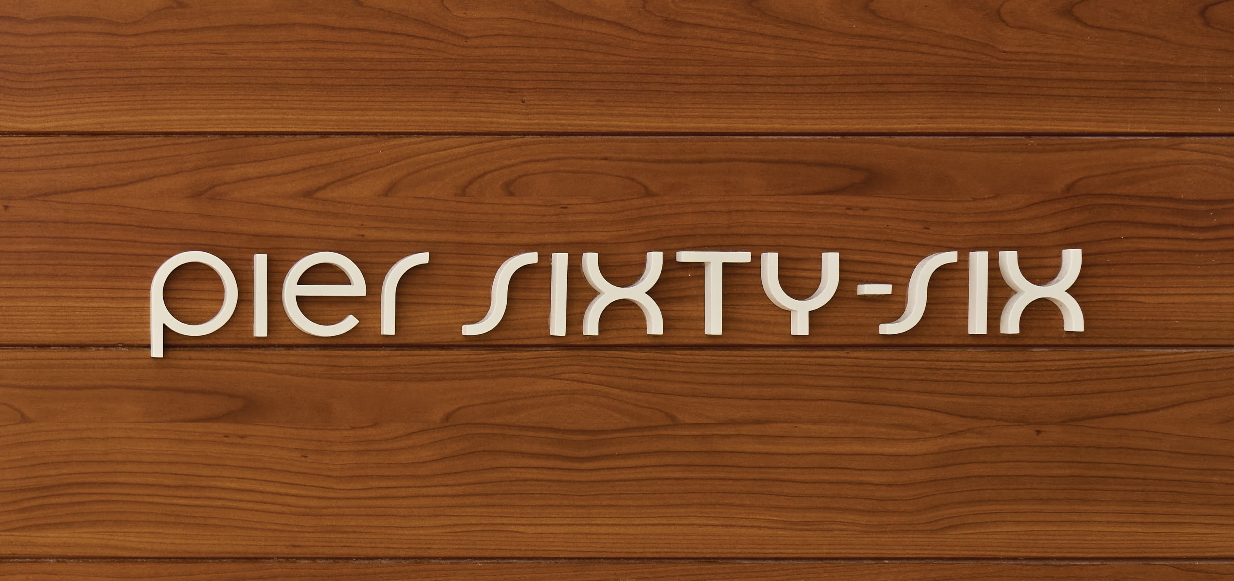Close-up detail of dimensional "Pier Sixty-Six" white letter signage mounted on a warm wood plank wall at Pier Sixty-Six luxury waterfront resort in Fort Lauderdale, Florida — RSM Design branding and visual identity, wayfinding and signage design, specialty graphics, and environmental graphic design for hospitality and waterfront destinations.