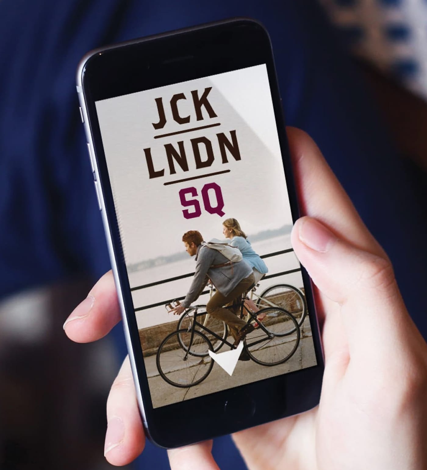 Smartphone displaying Jack London Square mobile branding with stacked “JCK LNDN SQ” logo and waterfront lifestyle imagery of cyclists riding along the Oakland, California marina promenade.