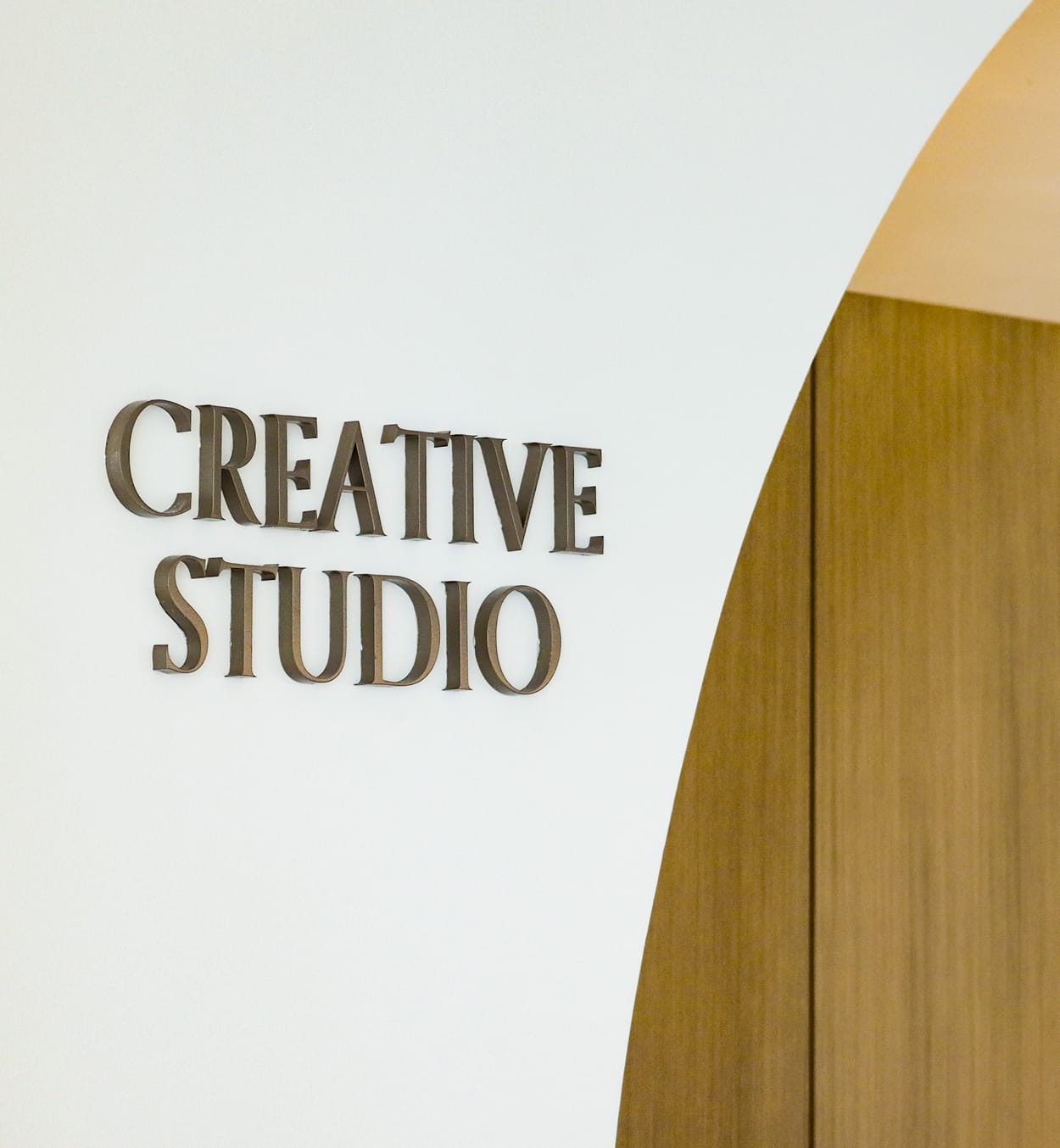 Bronze dimensional lettering reading "Creative Studio" beside an arched wood doorway at Maple Terrace - environmental graphic design by RSM Design
