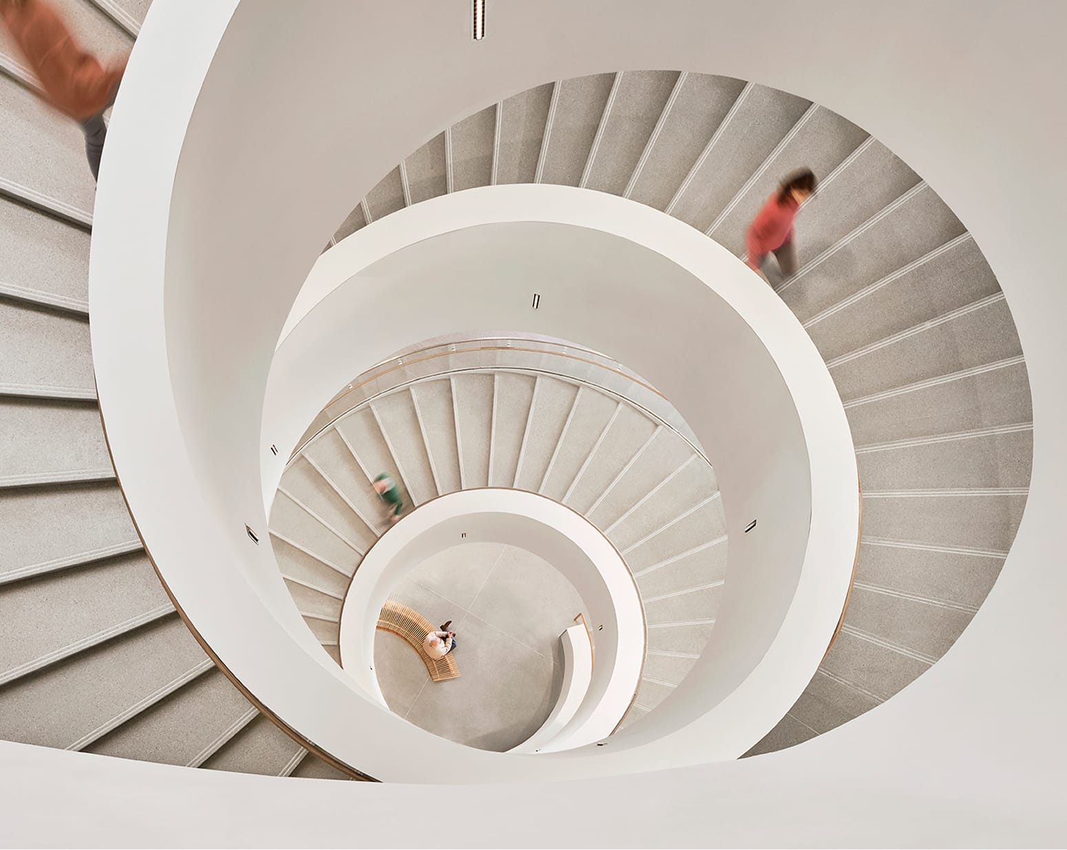 Dramatic overhead aerial view looking down a sculptural multi-story white spiral staircase with concentric circular landings and motion-blurred figures at Buddy Holly Hall of Performing Arts and Sciences, Lubbock Texas