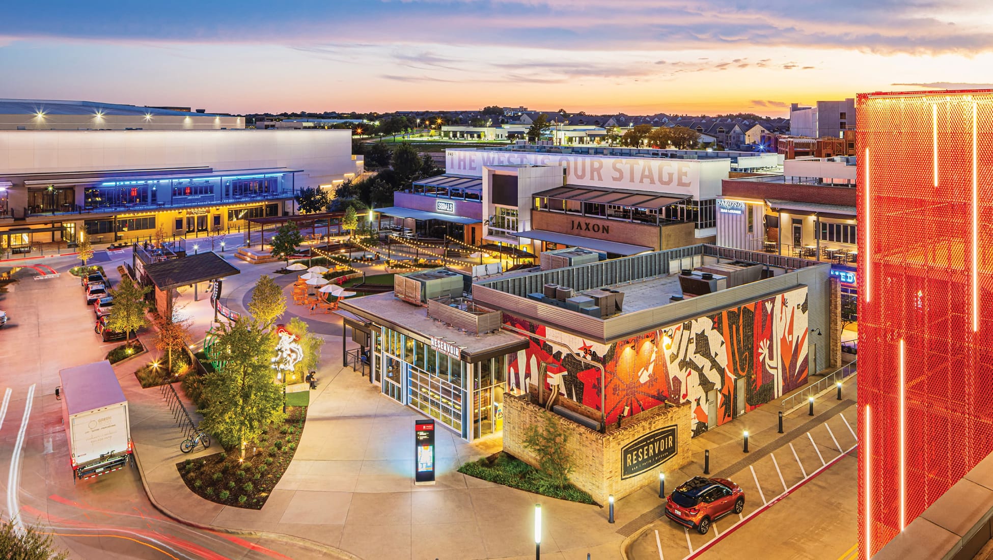Aerial dusk view of The Music Factory mixed-use entertainment district in Irving, Texas, featuring large-scale building murals, experiential graphics, environmental wayfinding signage, and placemaking design — RSM Design environmental graphic design for mixed-use, food and beverage, and retail destinations.