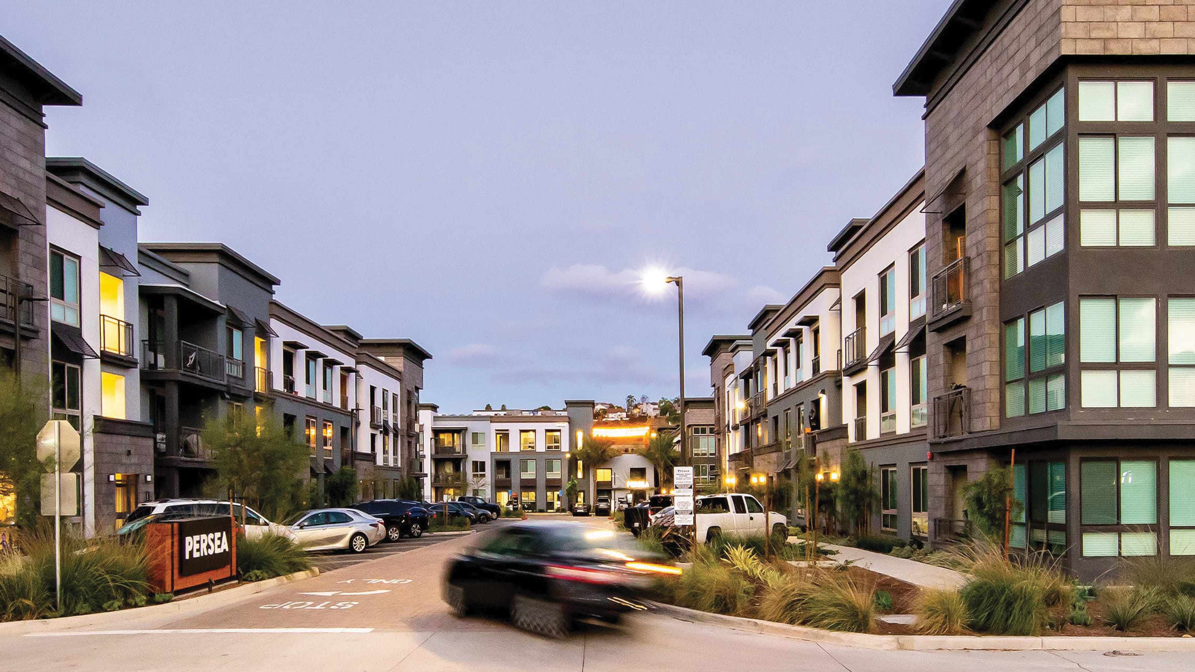 Mixed-use residential community streetscape with branded monument signage and integrated wayfinding, illustrating placemaking, environmental graphic design, and identity systems for multifamily housing, urban development, and lifestyle environments.