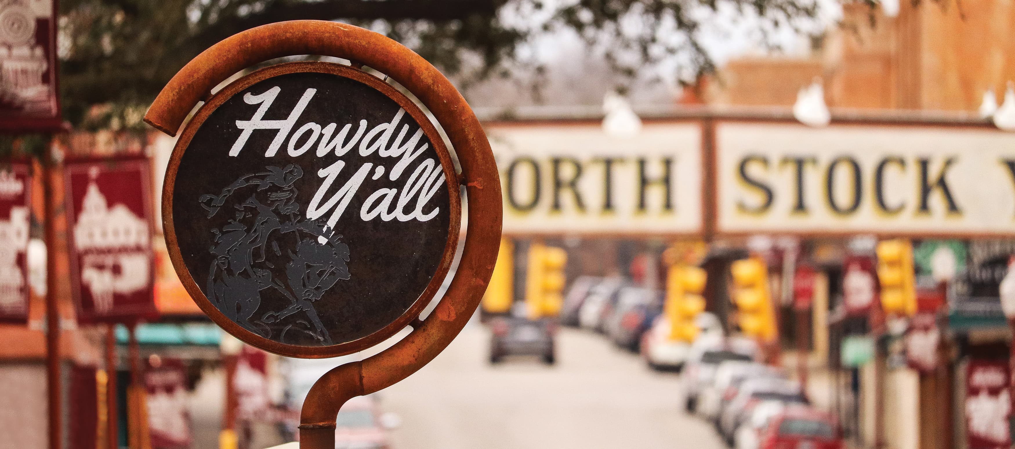 Close up of decorative sign reading, "Howdy Y'all" in front of Fort Worth Stockyards master sign.