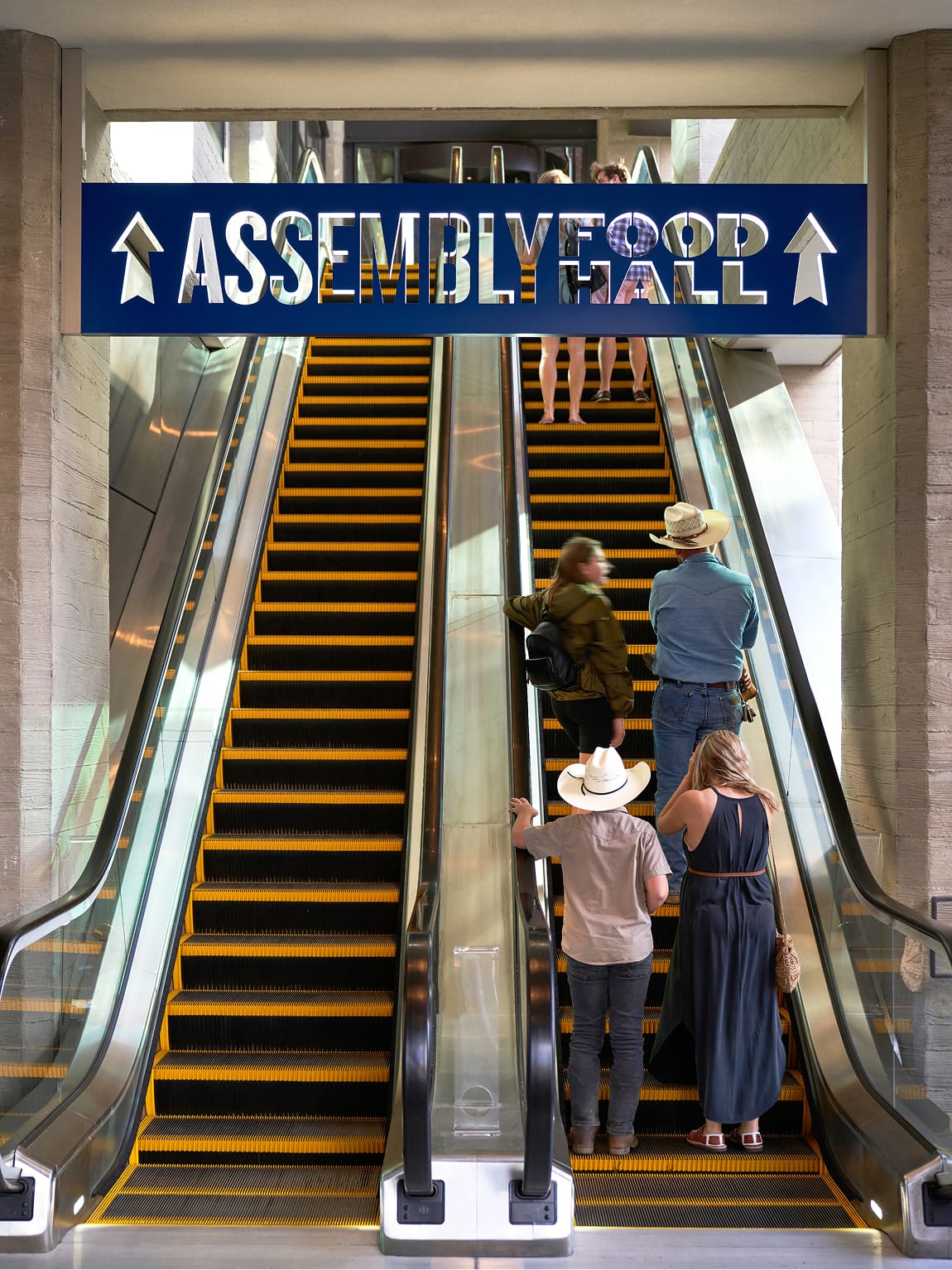 “Assembly Food Hall” overhead sign at Fifth + Broadway guiding visitors via escalators, providing clear directional wayfinding within the district.