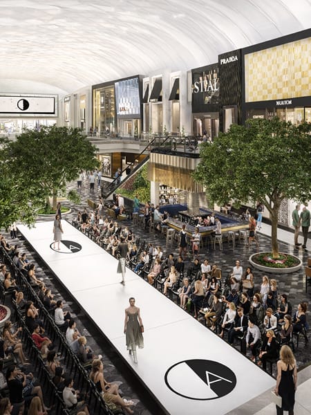 Architectural rendering of a fashion runway event in The Collections interior at American Dream mall in East Rutherford, New Jersey, featuring the American Dream logo mark repeated along a white runway floor, a vaulted ceiling atrium, multi-level luxury tenant storefronts including Prada, and an audience-filled experiential retail activation — showcasing RSM Design's experiential graphics, branded environments, and placemaking for a large-scale mixed-use luxury retail and entertainment destination.